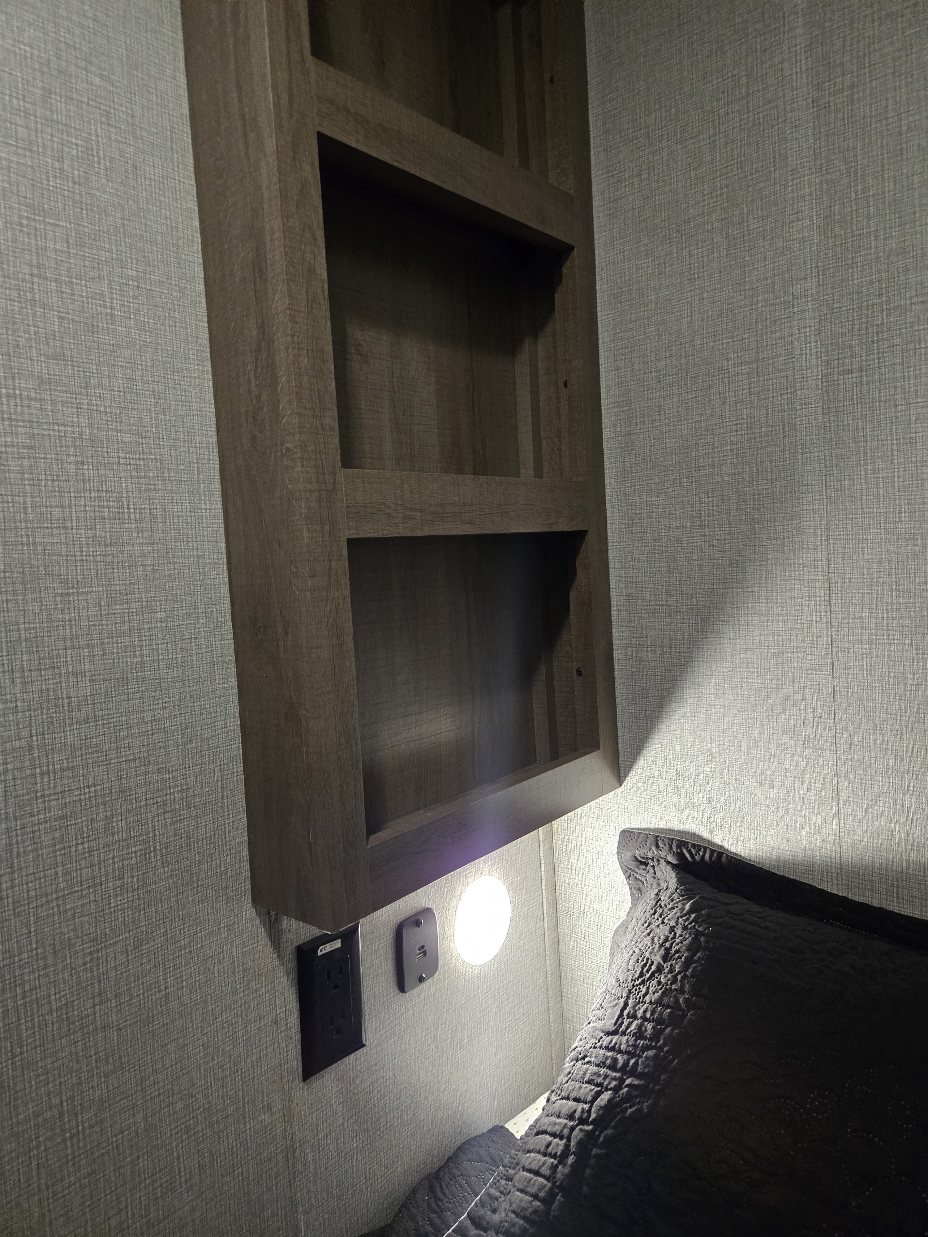 RV rental bedroom detail: clever storage with a bedside shelf, power outlet, USB, and light, beside a dark pillow.. Grand Design Imagine AIM 2023
