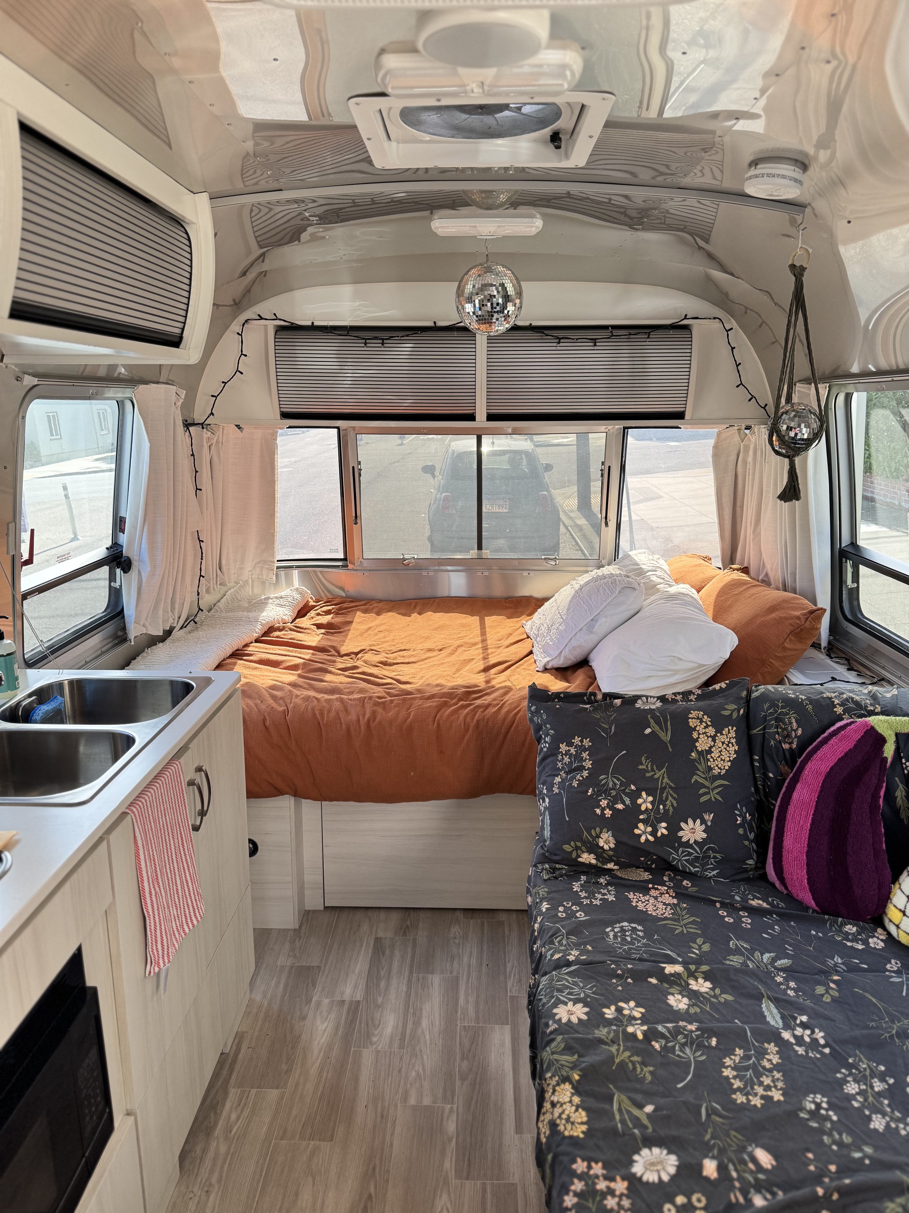 Inside this RV rental: a bright living space with a comfy bed, kitchen sink, and floral-patterned sofa for cozy trips.. Airstream Bambi 2023