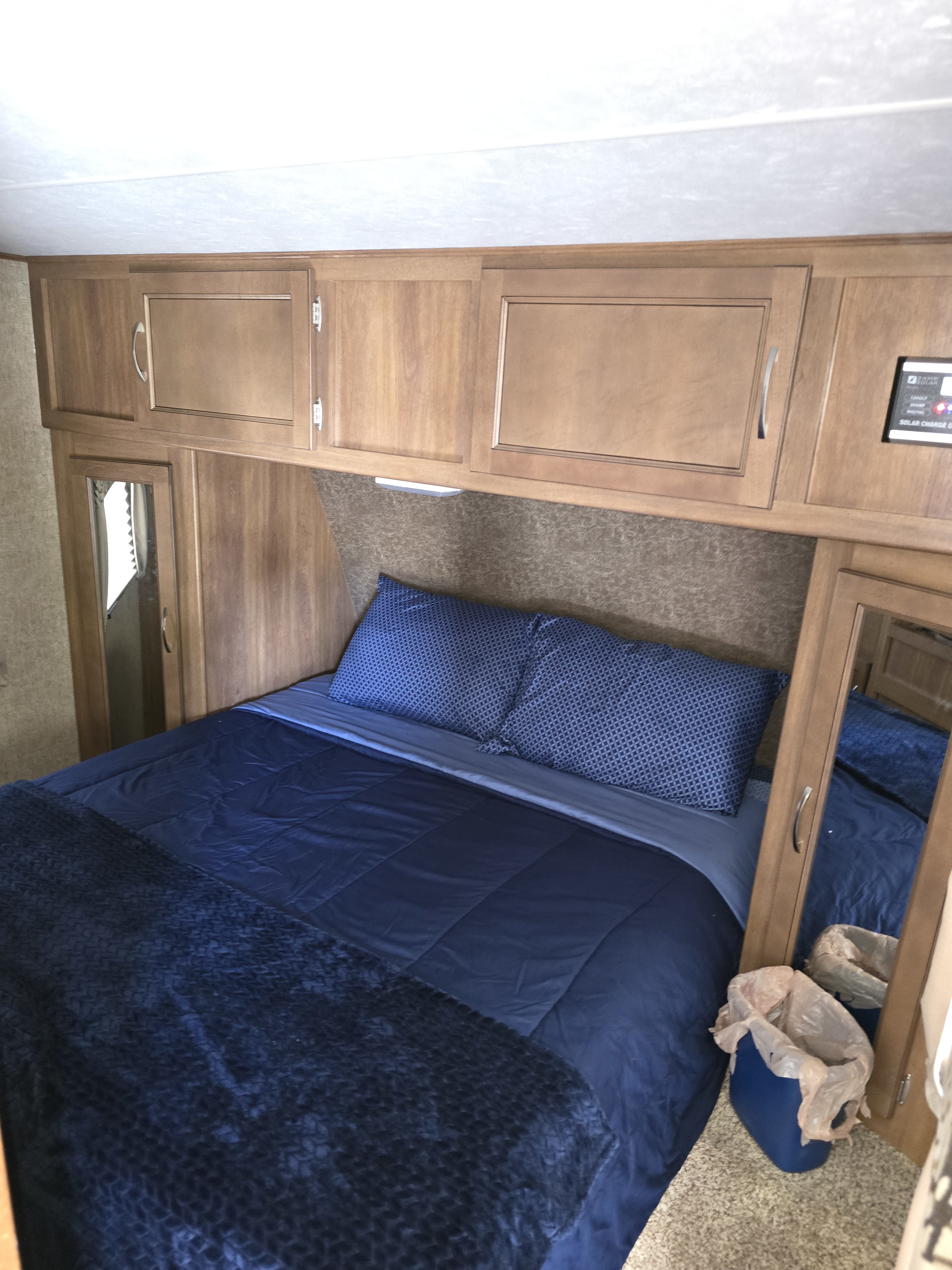 Comfortable RV rental bedroom with blue bed, overhead cabinets, essential controls, and a mirror.. Coachmen Apex 2015