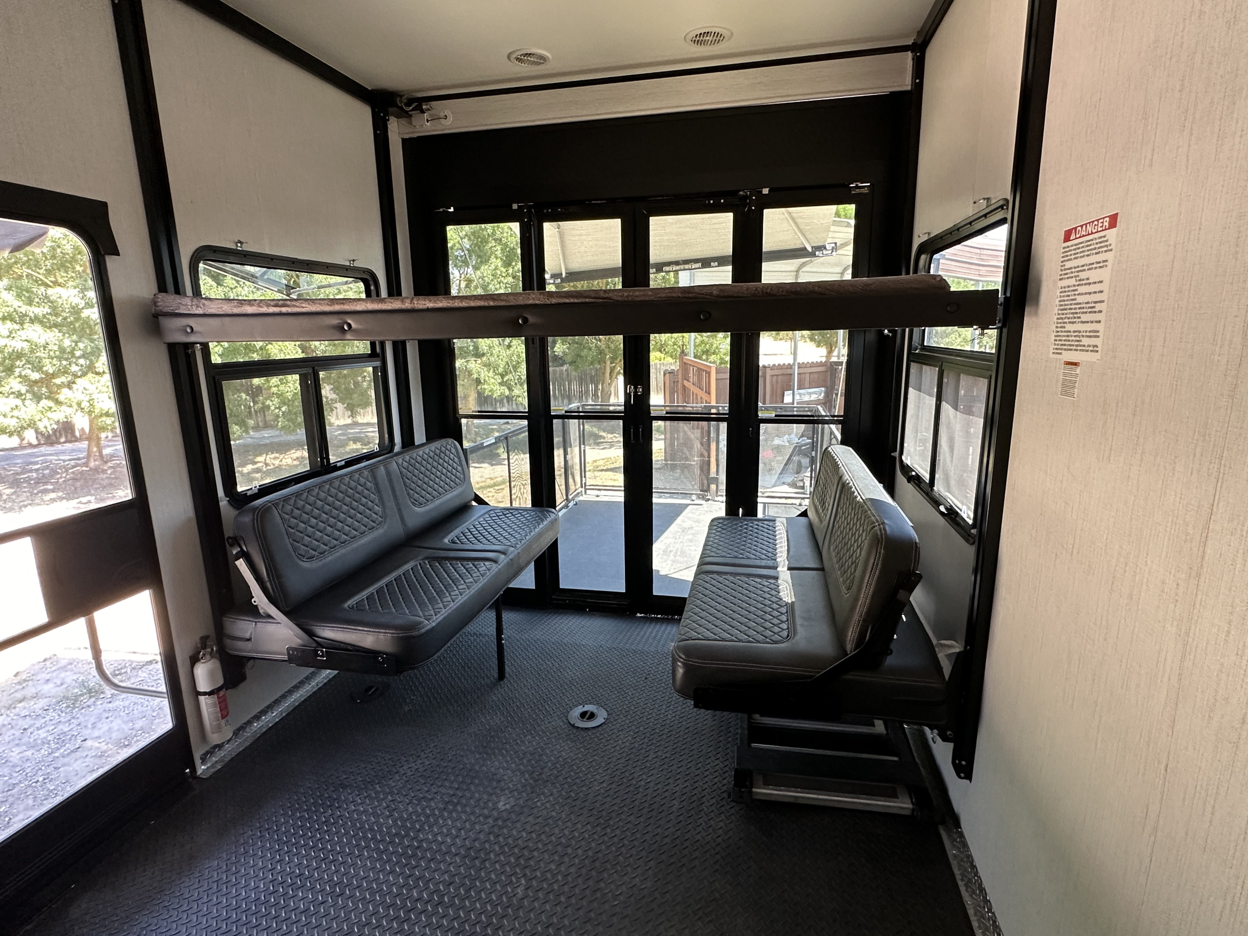 RV rental toy hauler interior: convertible benches, suspended bunk, and open rear ramp door to nature.. Heartland RVs Road Warrior Toy Hauler 2022