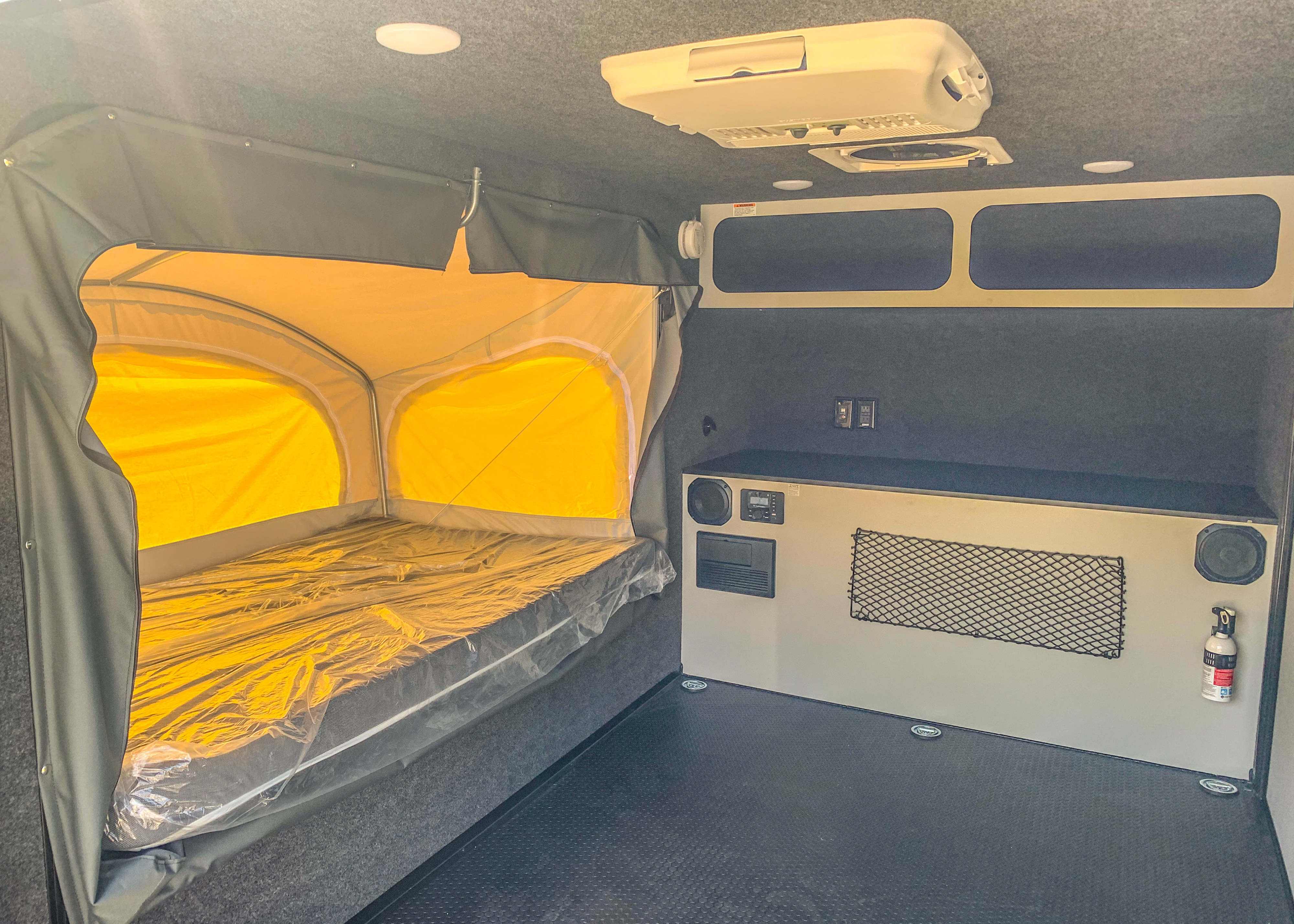 Interior of an RV rental showing a pop-out bed, equipped utility wall with outlets/speakers, and overhead AC.. Intech Explorer 2021