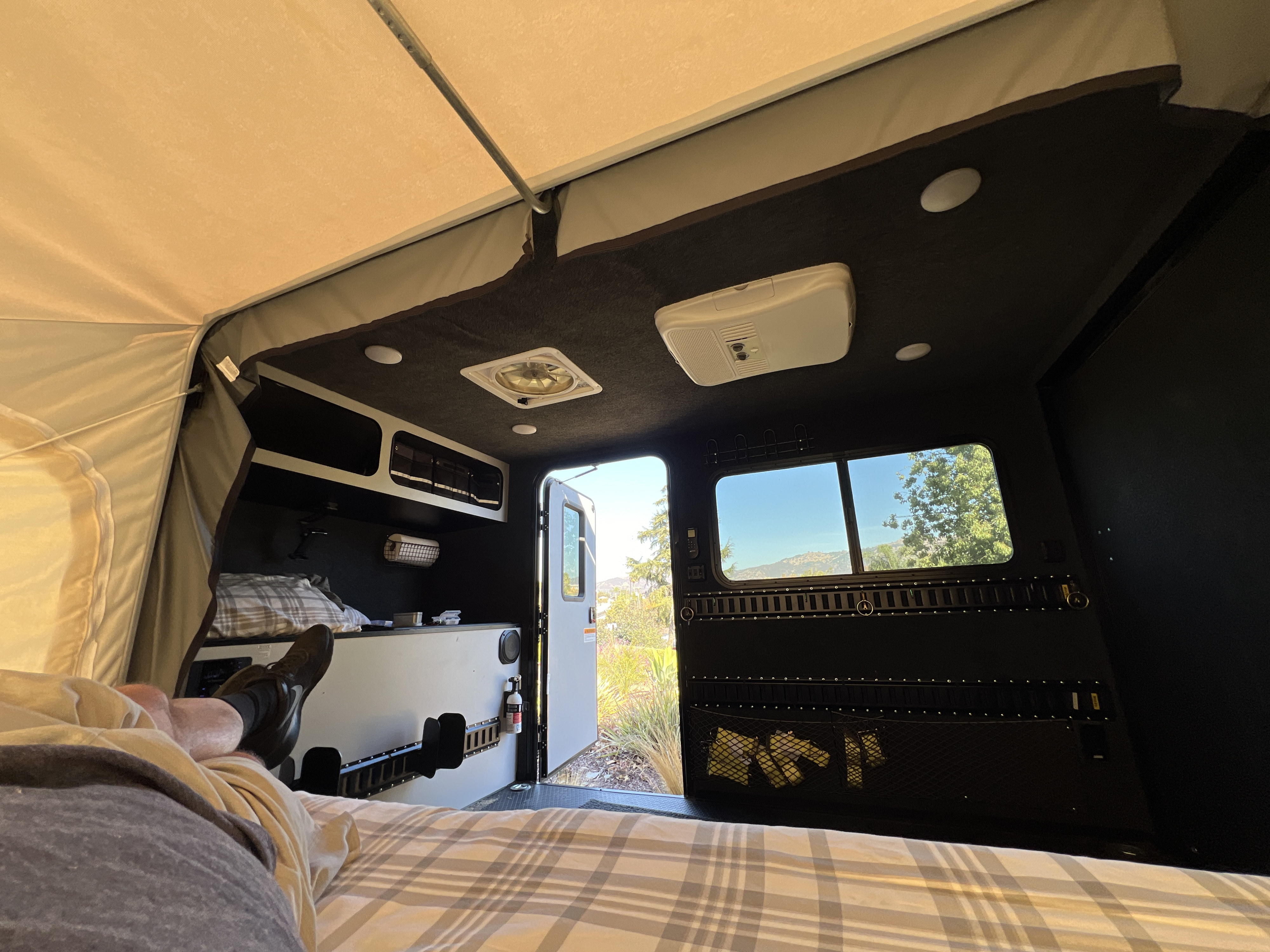Inside a comfy RV rental: person relaxing on bed, looking out at nature through open door & windows. Great for camping!. Intech Explorer 2021