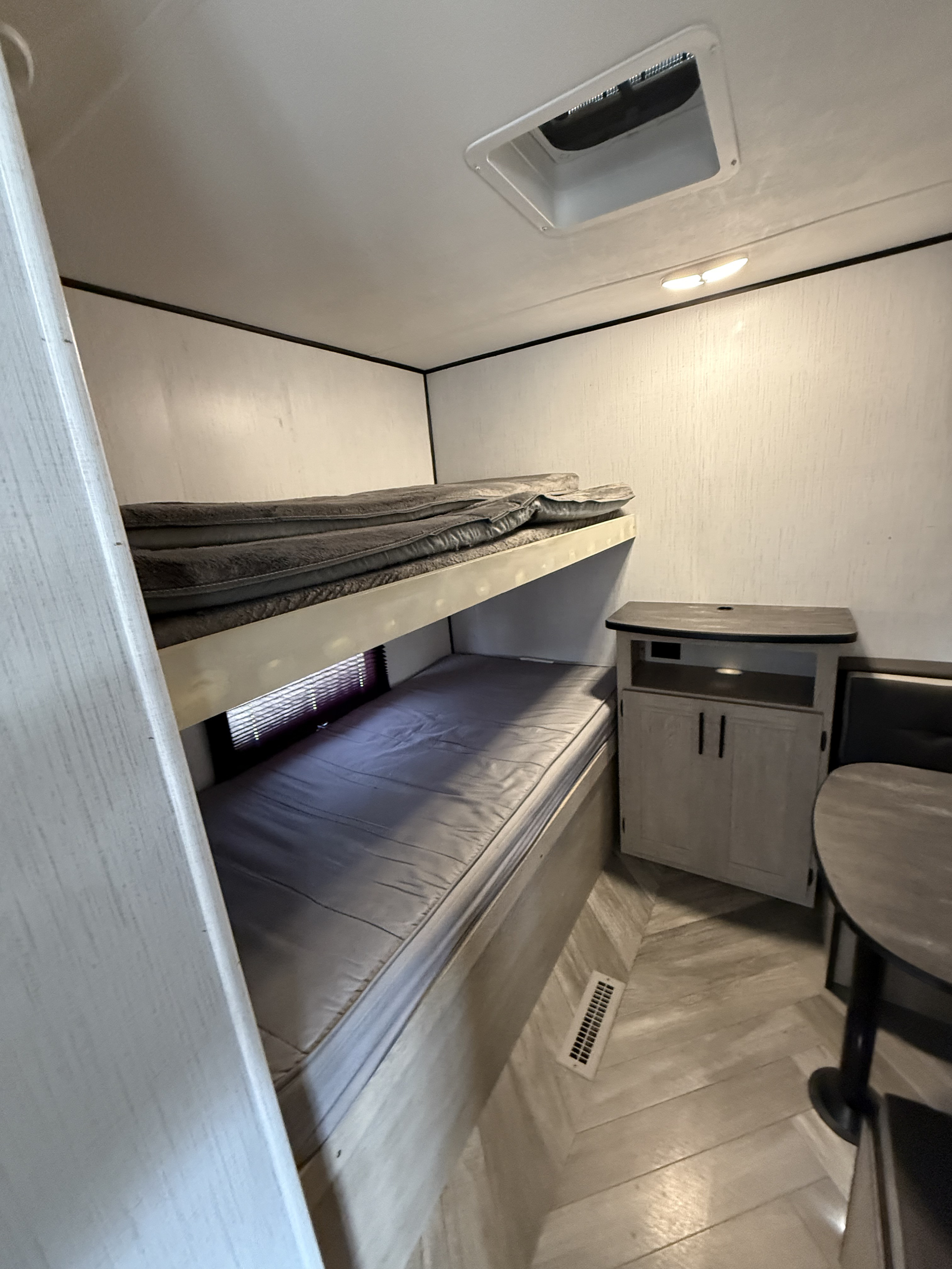 Cozy RV rental interior with bunk beds, dining table, storage cabinet, and herringbone flooring. Ideal for family trips.. Heartland RVs Prowler 2021