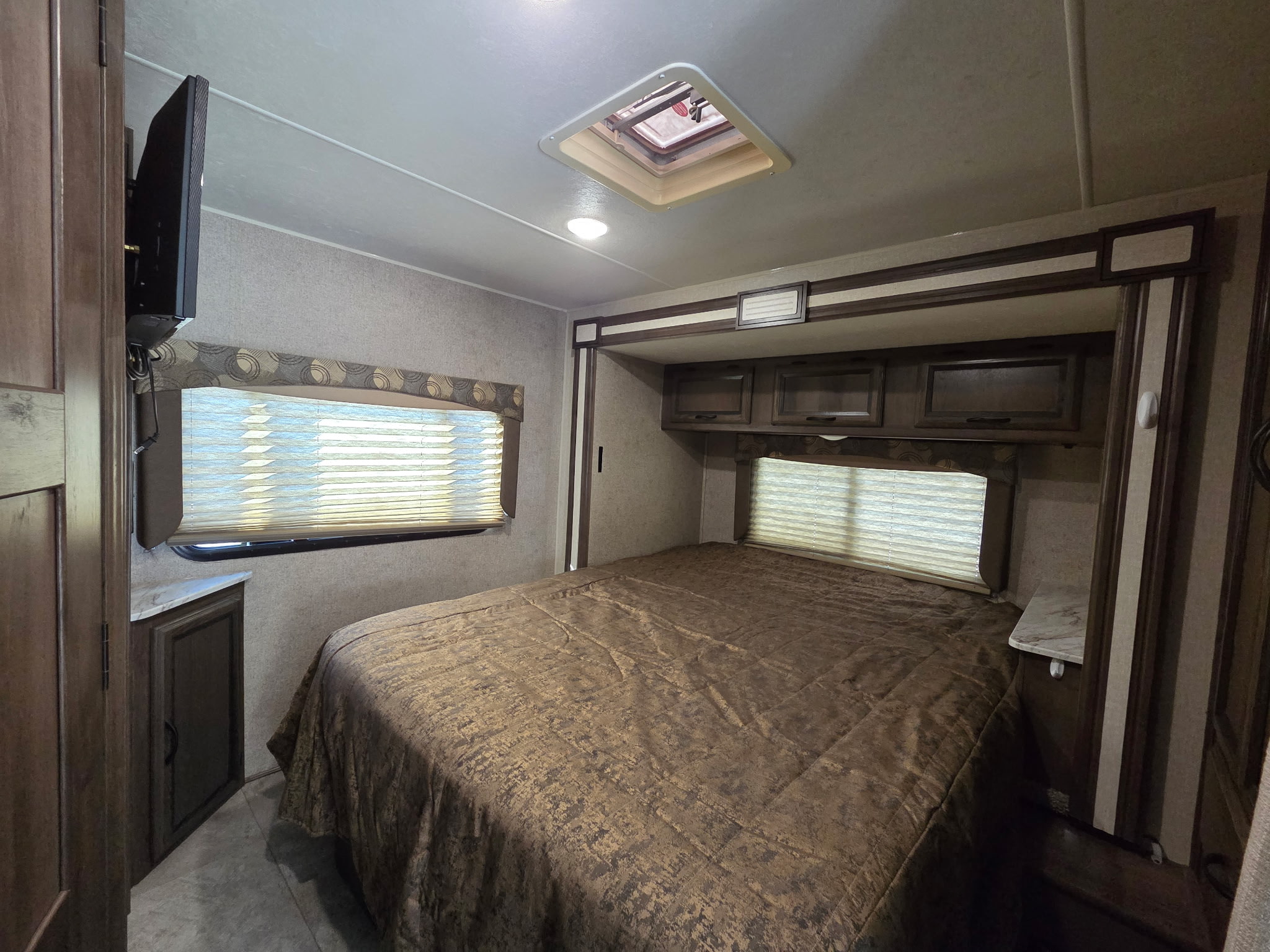 Spacious RV rental bedroom with a comfortable bed, overhead storage, mounted TV, and natural light from windows and ceiling vent.. Forest River Coachmen Freelander 2019