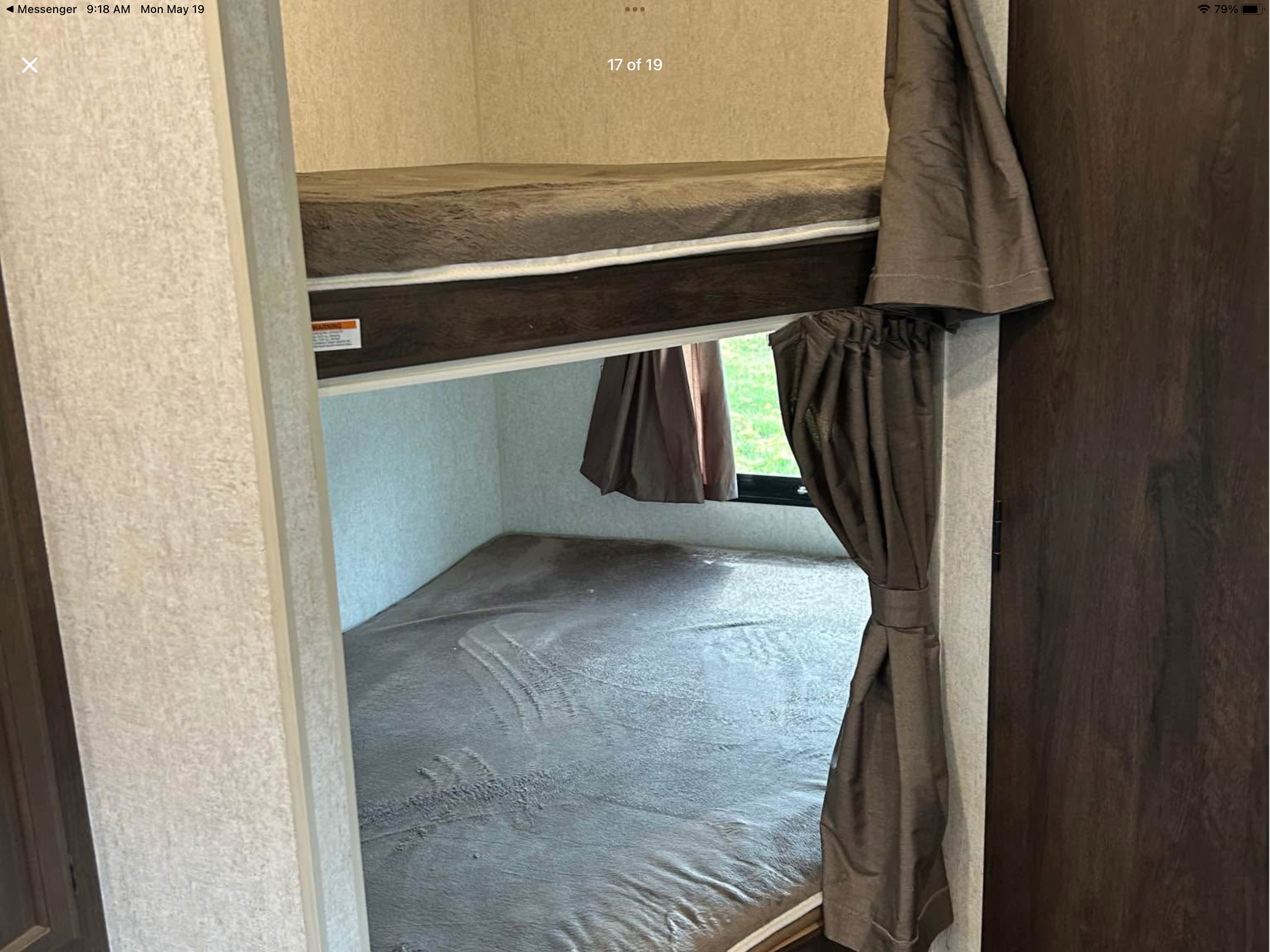 Inside an RV rental, showing the lower and upper bunk beds with brown curtains and a window view.. Starcraft Avalon 2018