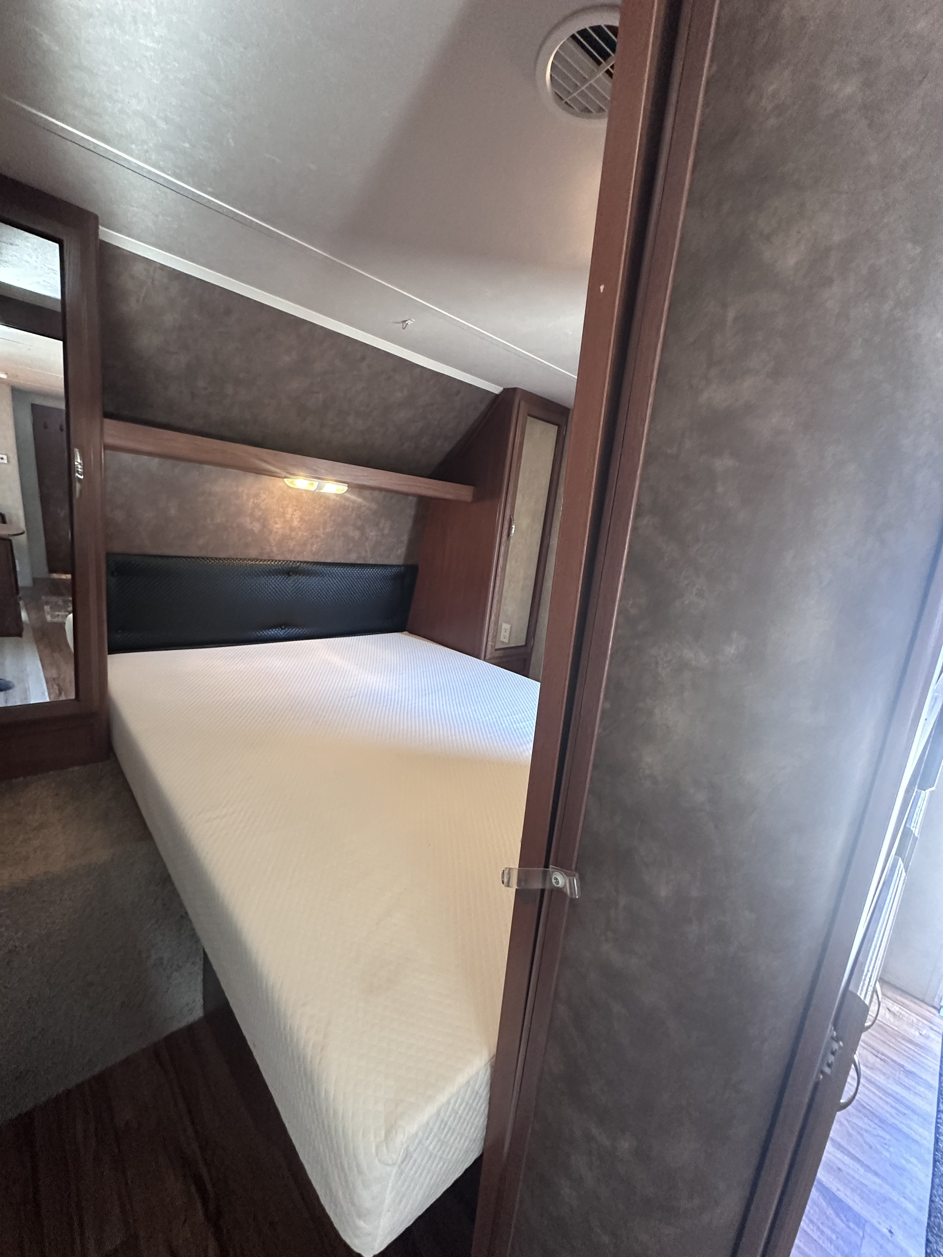 Cozy RV rental bedroom featuring a large white mattress, black headboard, and functional overhead lighting.. Forest River Wildwood 2014