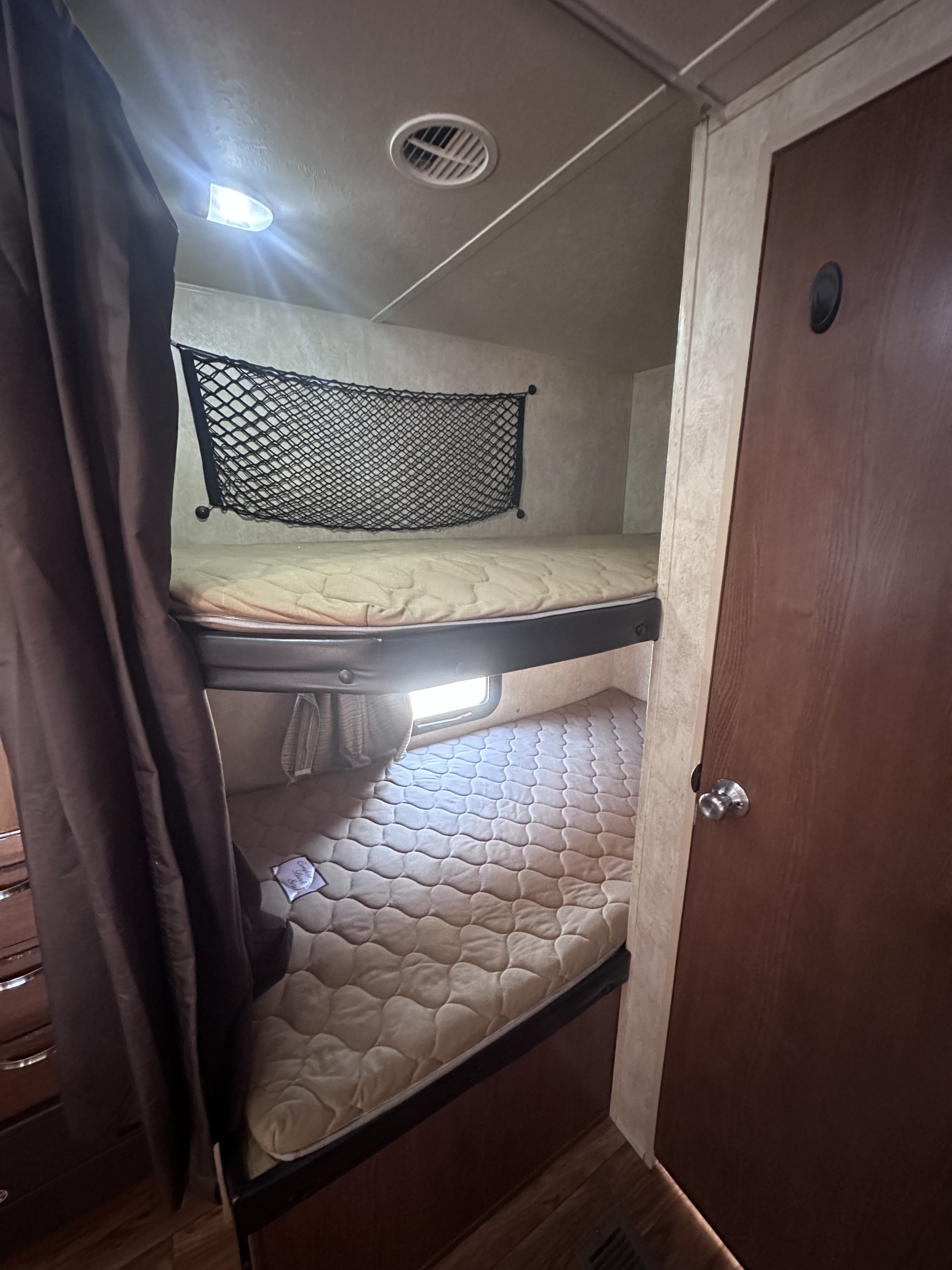 Cozy bunk beds in an RV rental, featuring quilted mattresses, a privacy curtain, storage net, and a window.. Forest River Wildwood 2014