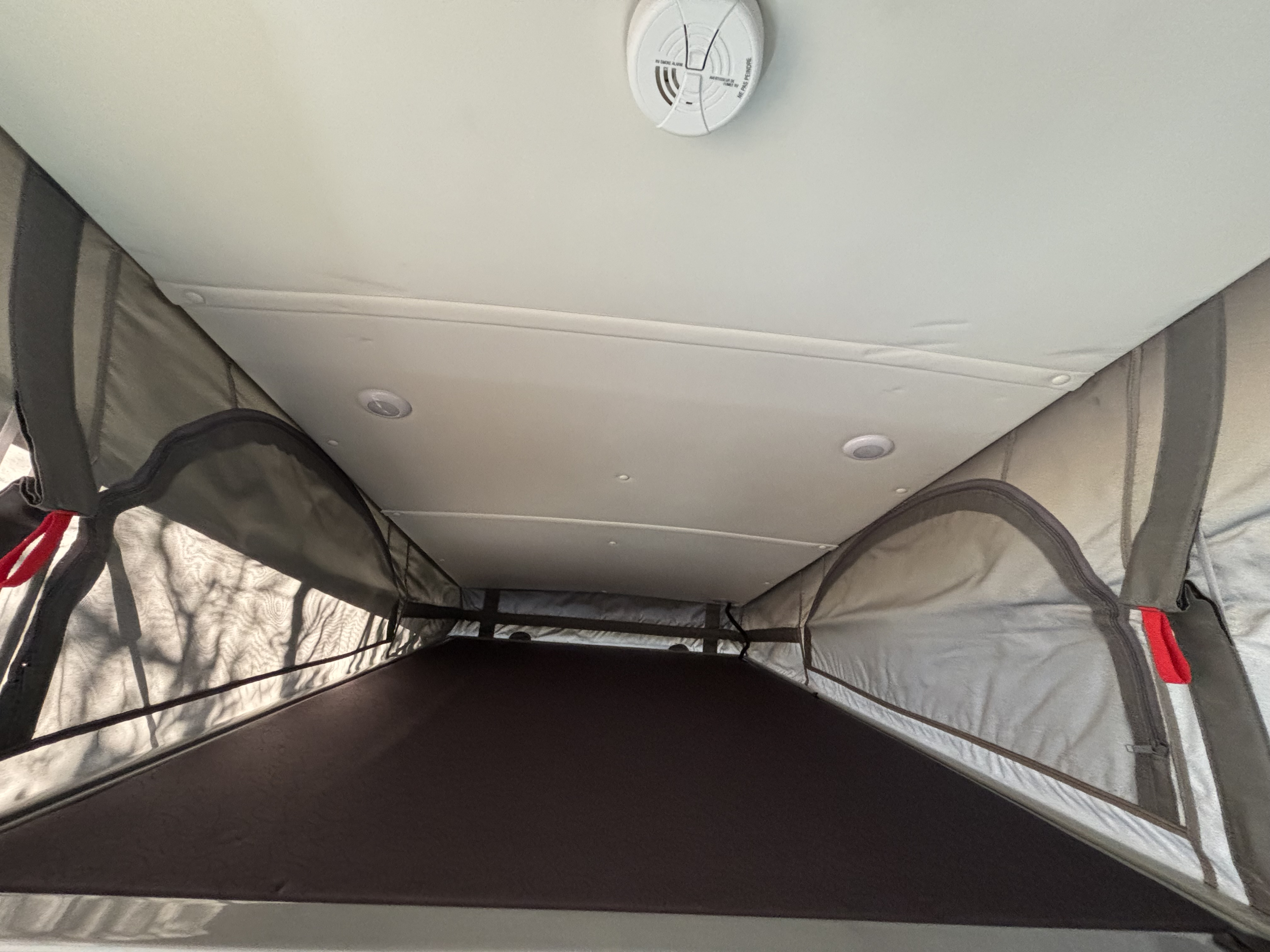 Overhead view inside an RV rental pop-top with a bed, ceiling-mounted smoke detector, and recessed lighting.. Pleasure Way Tofino 2022