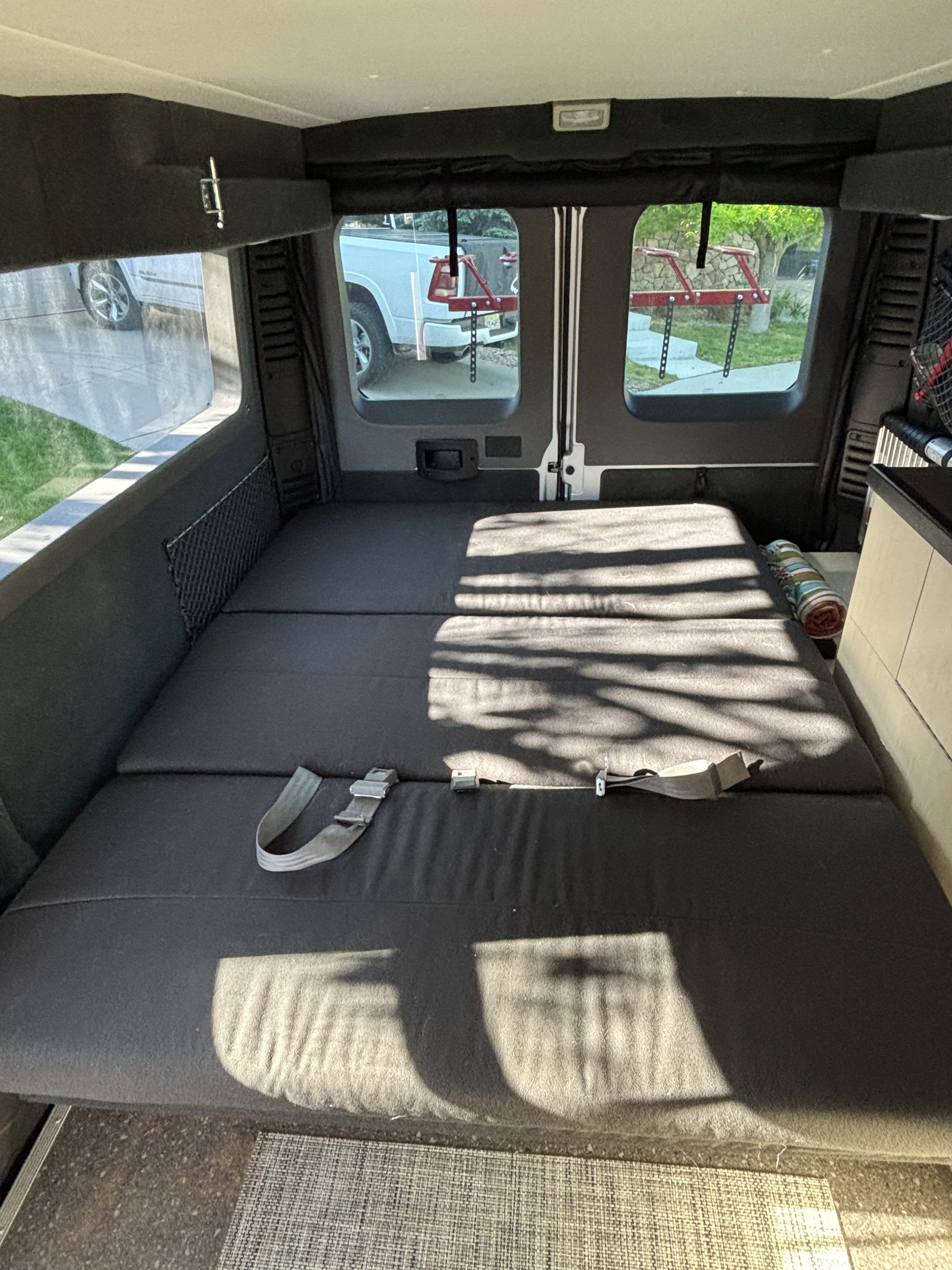 Inside this RV rental, see the comfy convertible bed with seatbelts, ambient sunlight, and clear window views.. Pleasure Way Tofino 2022