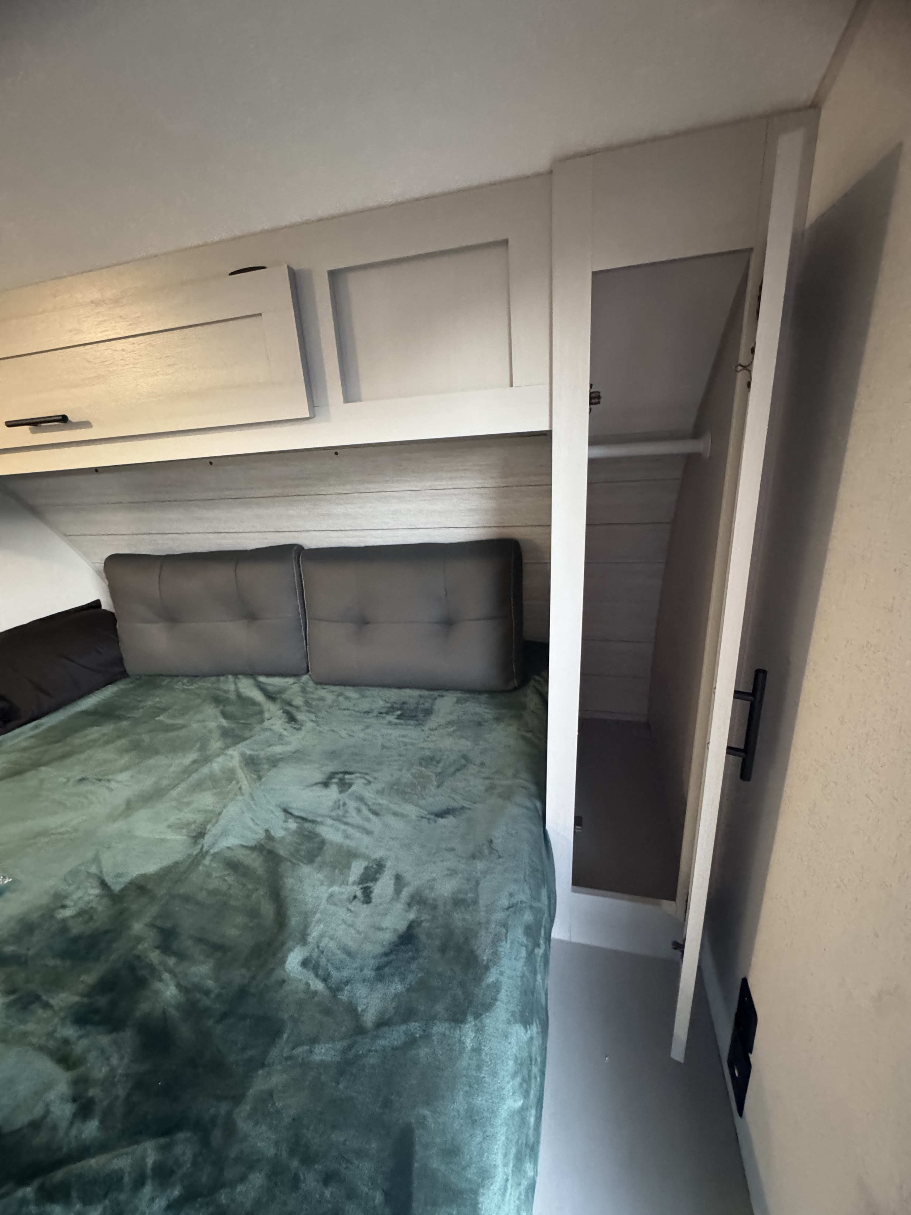 RV rental bedroom featuring a comfy bed, overhead storage, and an open closet with a hanging rod.. Forest River Wildwood FSX 2021