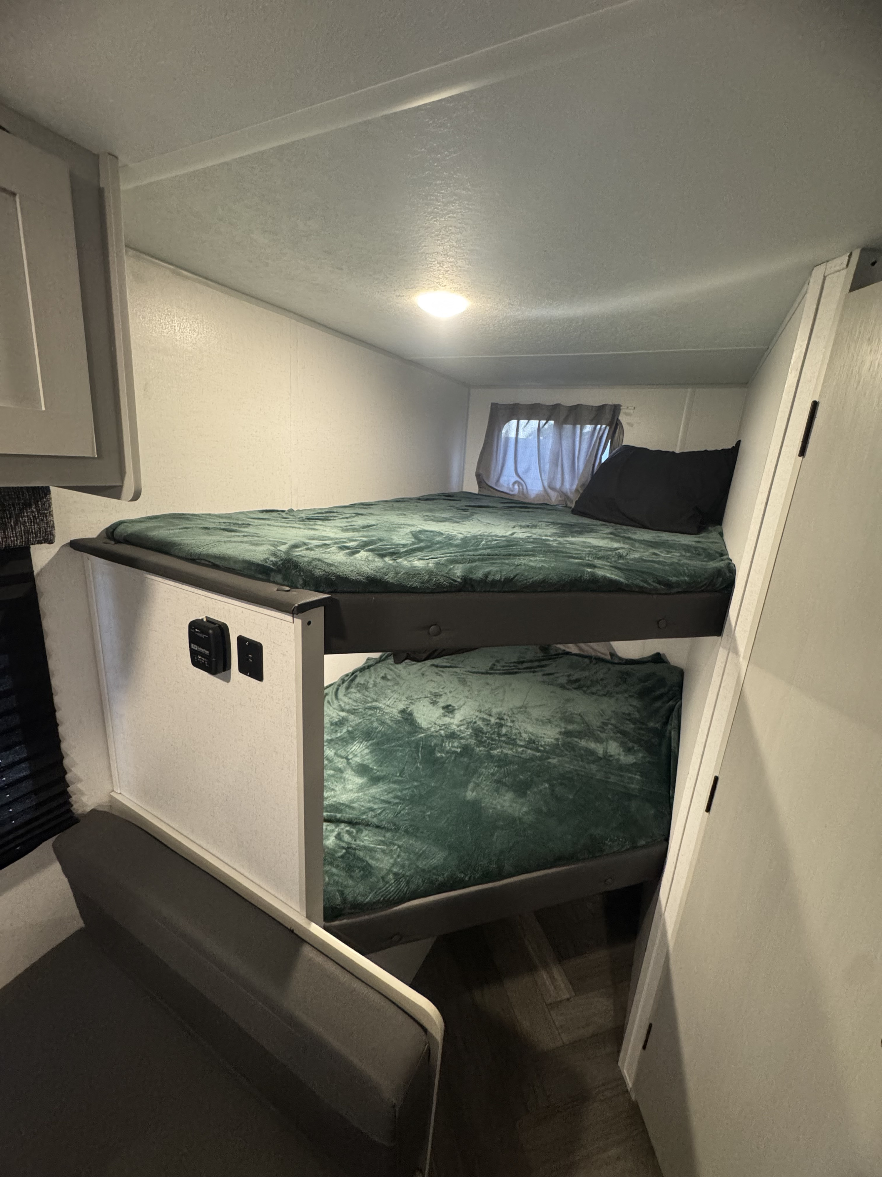 Inside an RV rental: two compact bunk beds with soft green blankets. Perfect for family adventures.. Forest River Wildwood FSX 2021