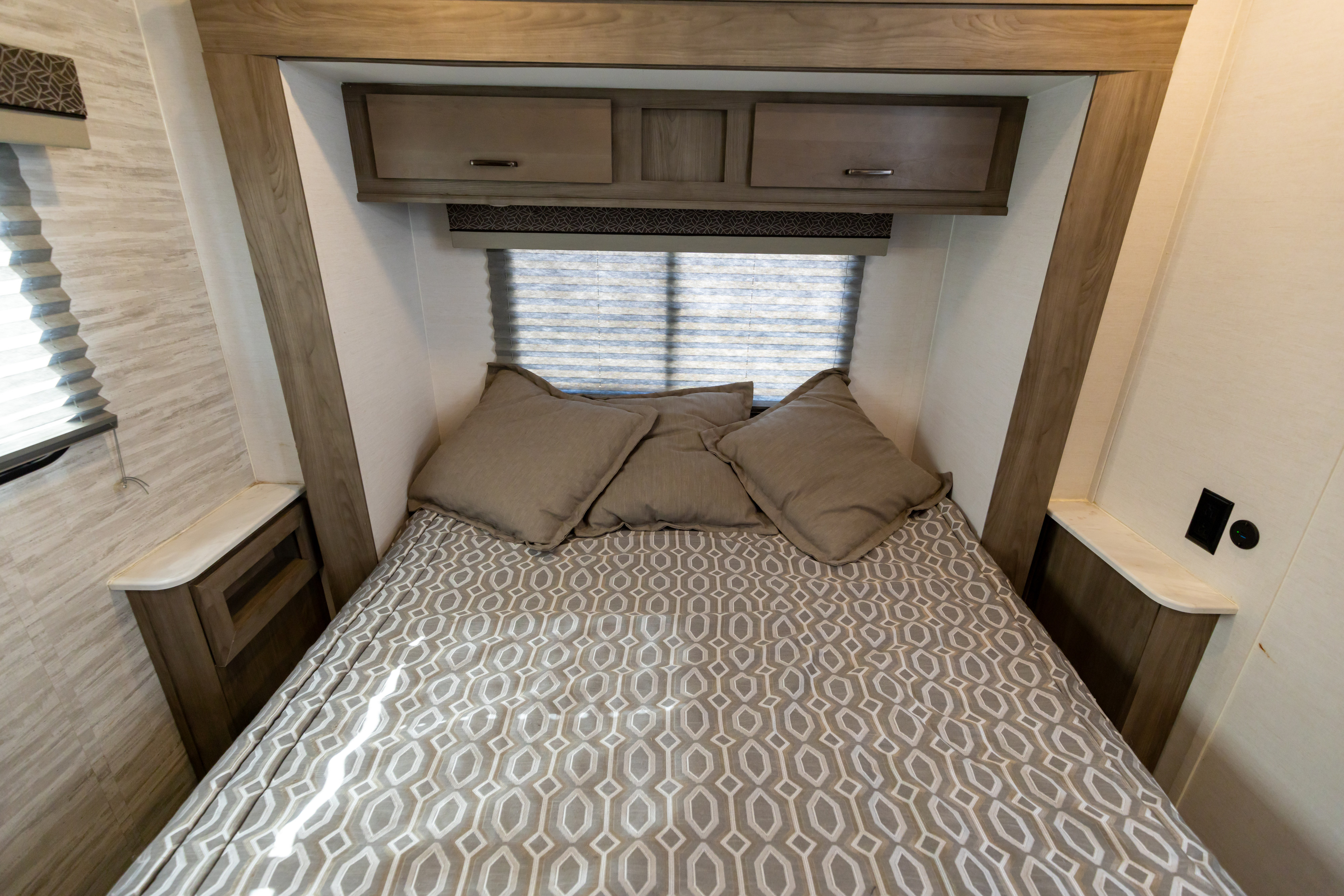 Cozy RV rental bedroom featuring patterned bedding, overhead cabinets, window blinds, and compact bedside tables.. Gulf Stream Conquest 2024