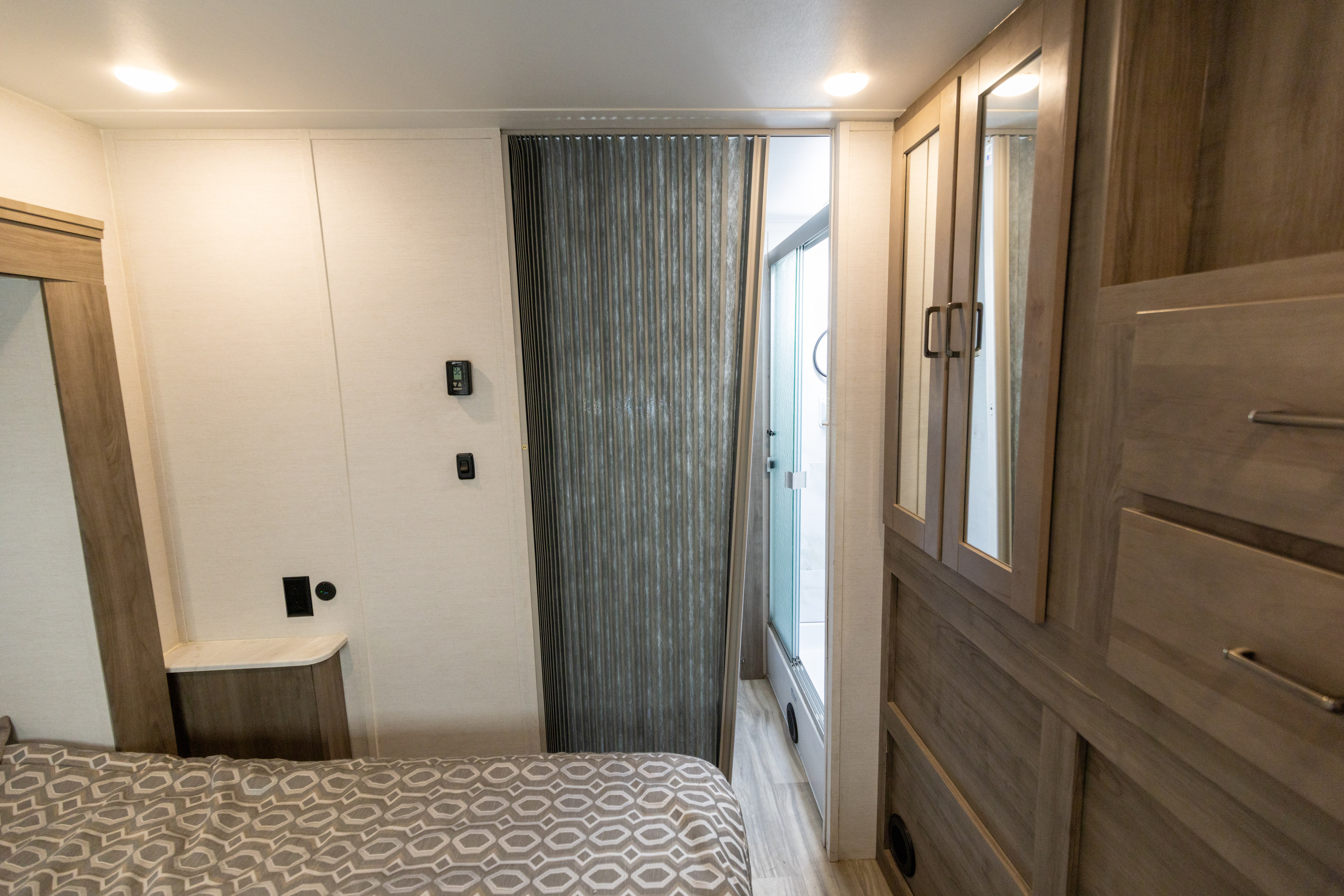 Inside an RV rental: a modern bedroom with bed, built-in storage, and a folding door leading to the shower bath.. Gulf Stream Conquest 2024