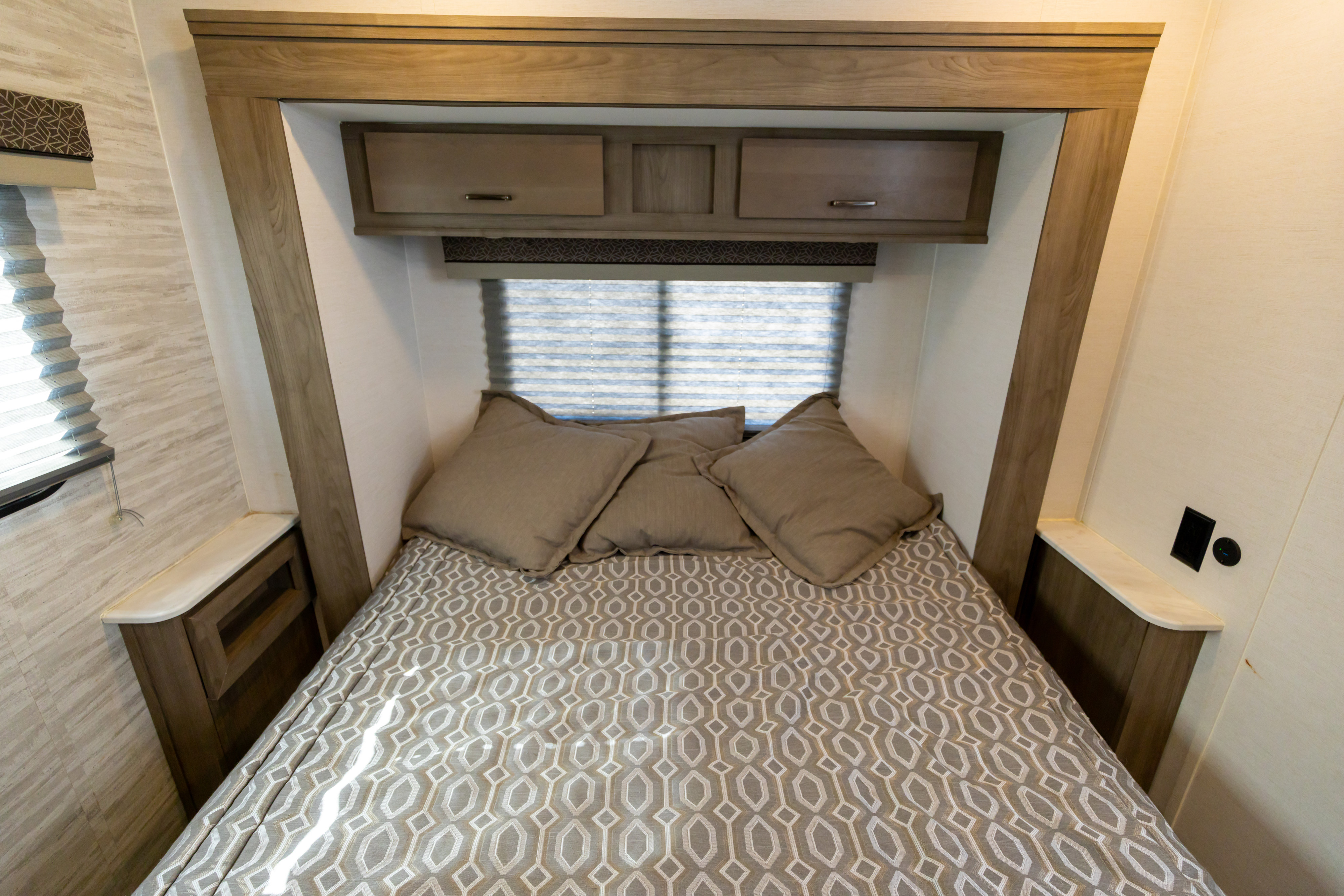 Modern RV rental bedroom with a comfy bed, neutral patterned bedding, and practical overhead and side cabinets.. Gulf Stream Conquest 2024