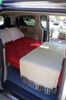 Transforming travel: See inside this RV rental minivan camper with a comfy bed, red blanket, and pillows, ready for adventure.. Dodge Grand Caravan 2012
