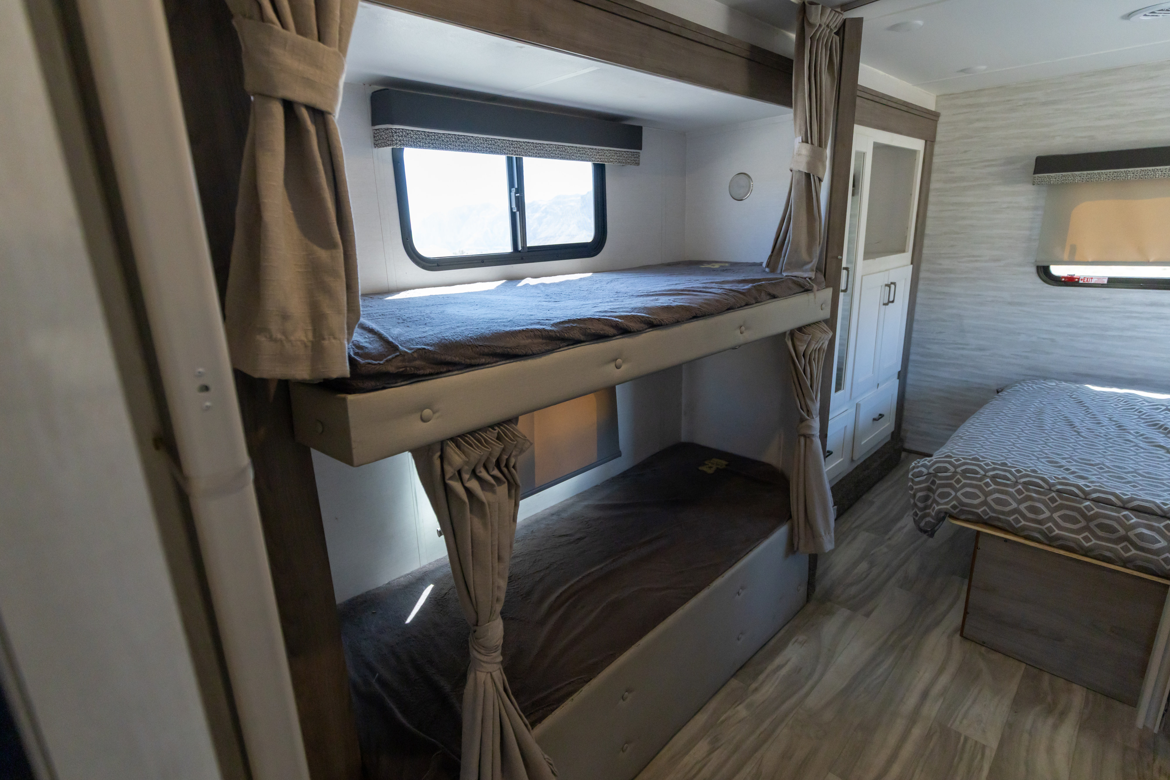 Functional RV rental bedroom showcasing bunk beds, a main bed, and sleek white storage.. Gulf Stream Conquest 2023