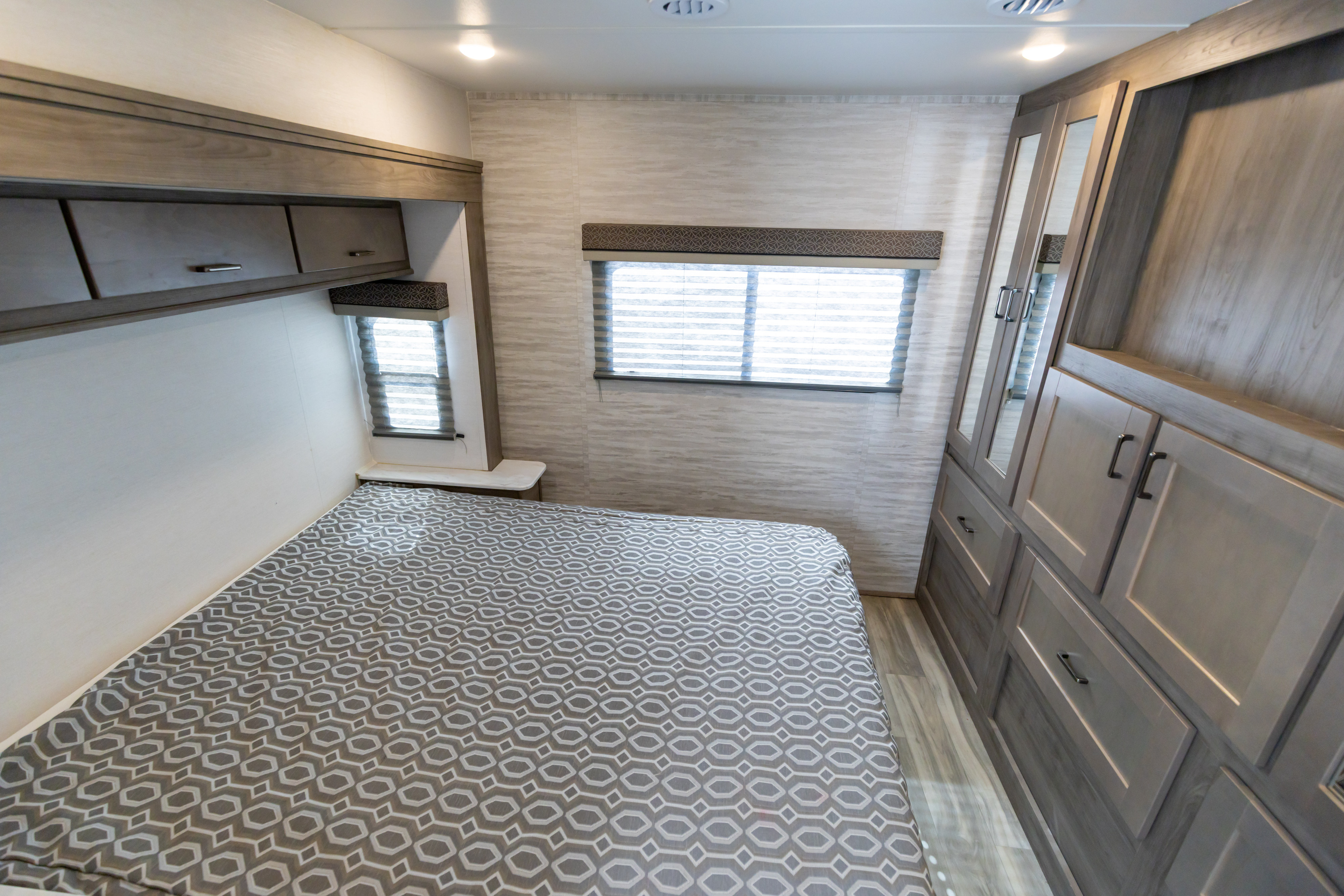 Modern RV rental bedroom featuring a comfortable bed, convenient overhead storage, windows with blinds, and built-in closet space.. Gulf Stream Conquest 2024