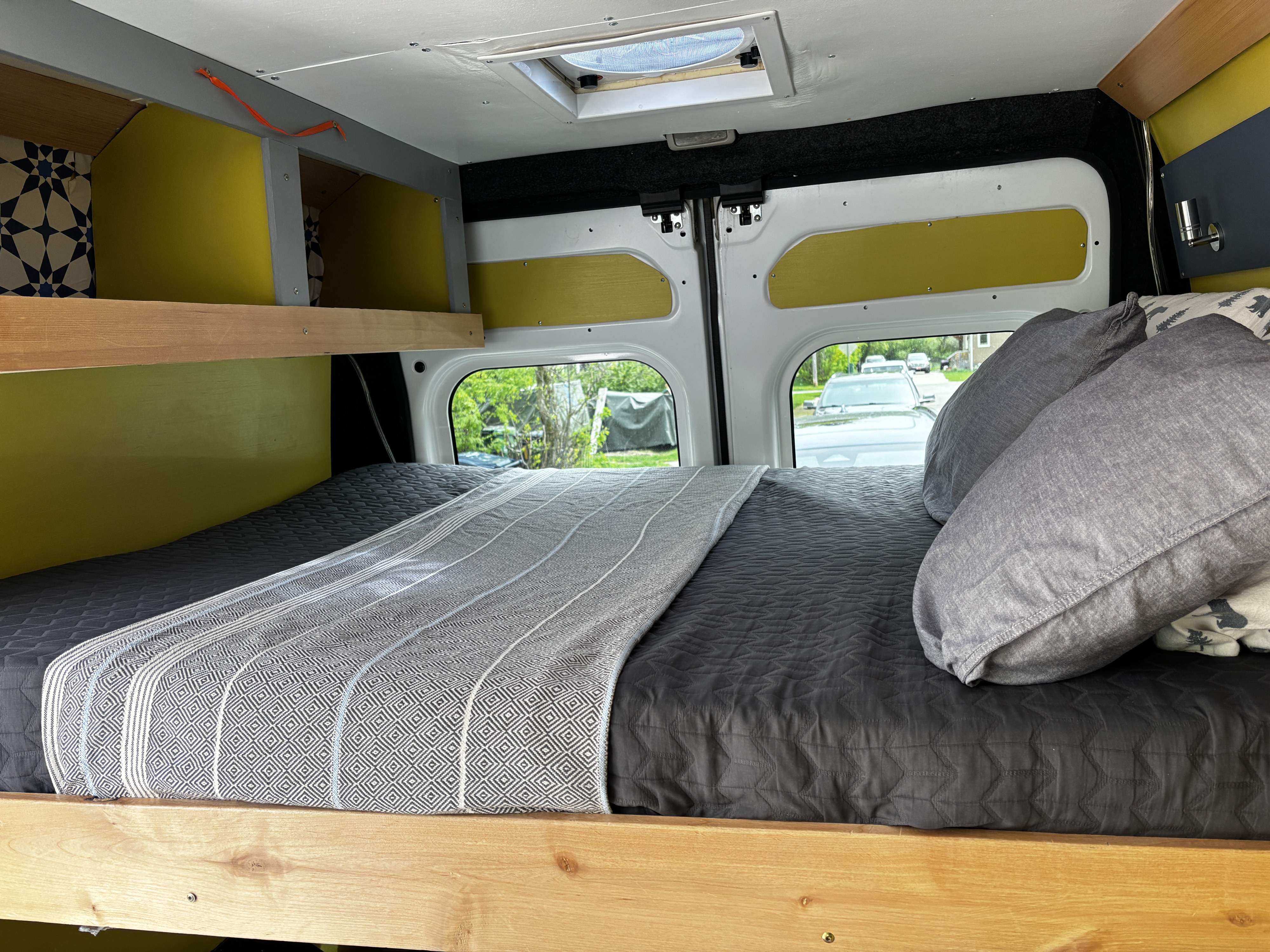 Cozy camper van RV rental interior: A bed with grey bedding, wood accents, built-in shelves & rear view windows.. RAM Promaster 1500 2020