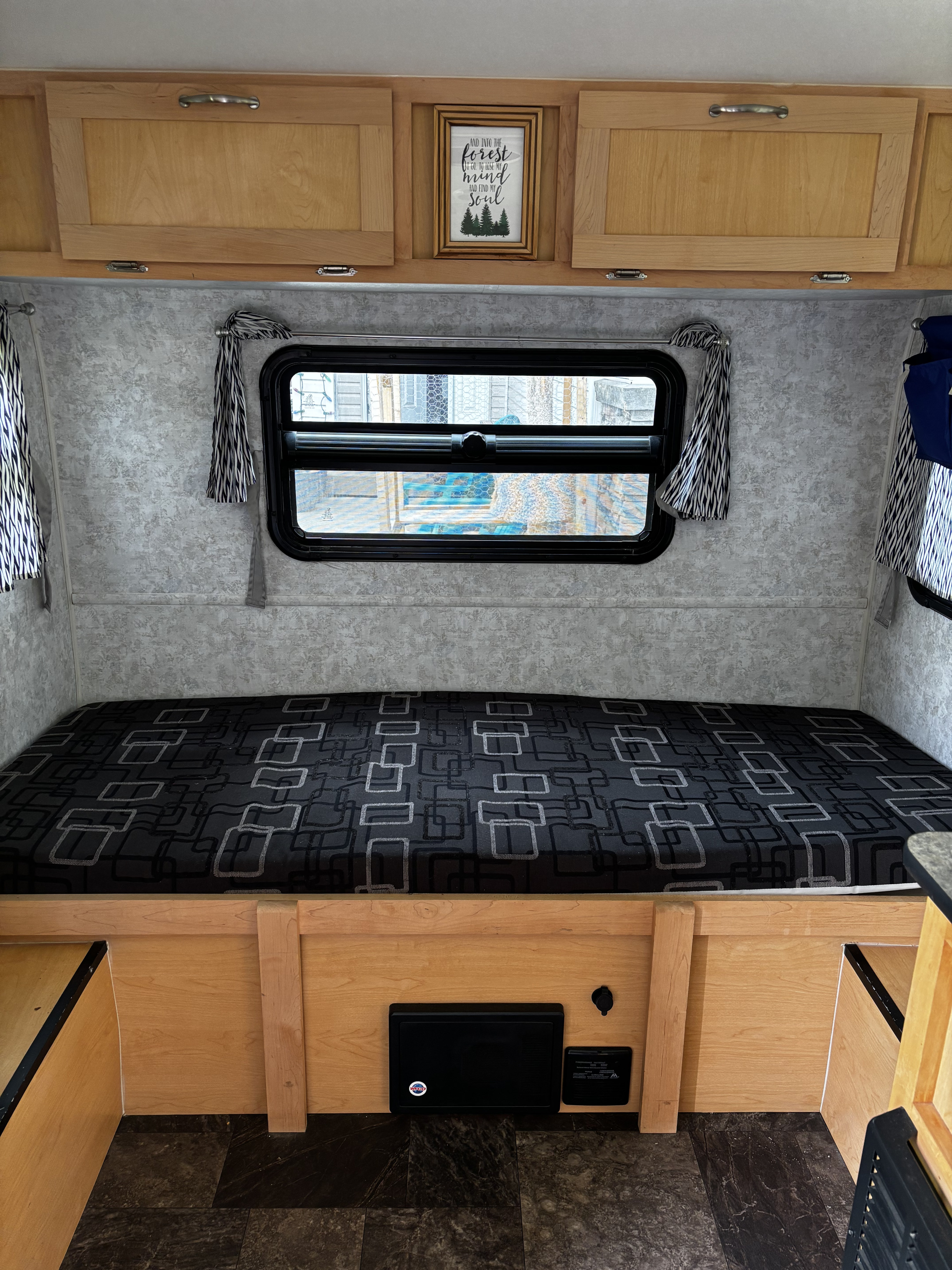 RV rental interior: cozy bed with geometric pattern, wood cabinets, and 'forest' framed art. Your adventure awaits!. Prolite Prolite Trailer 2017