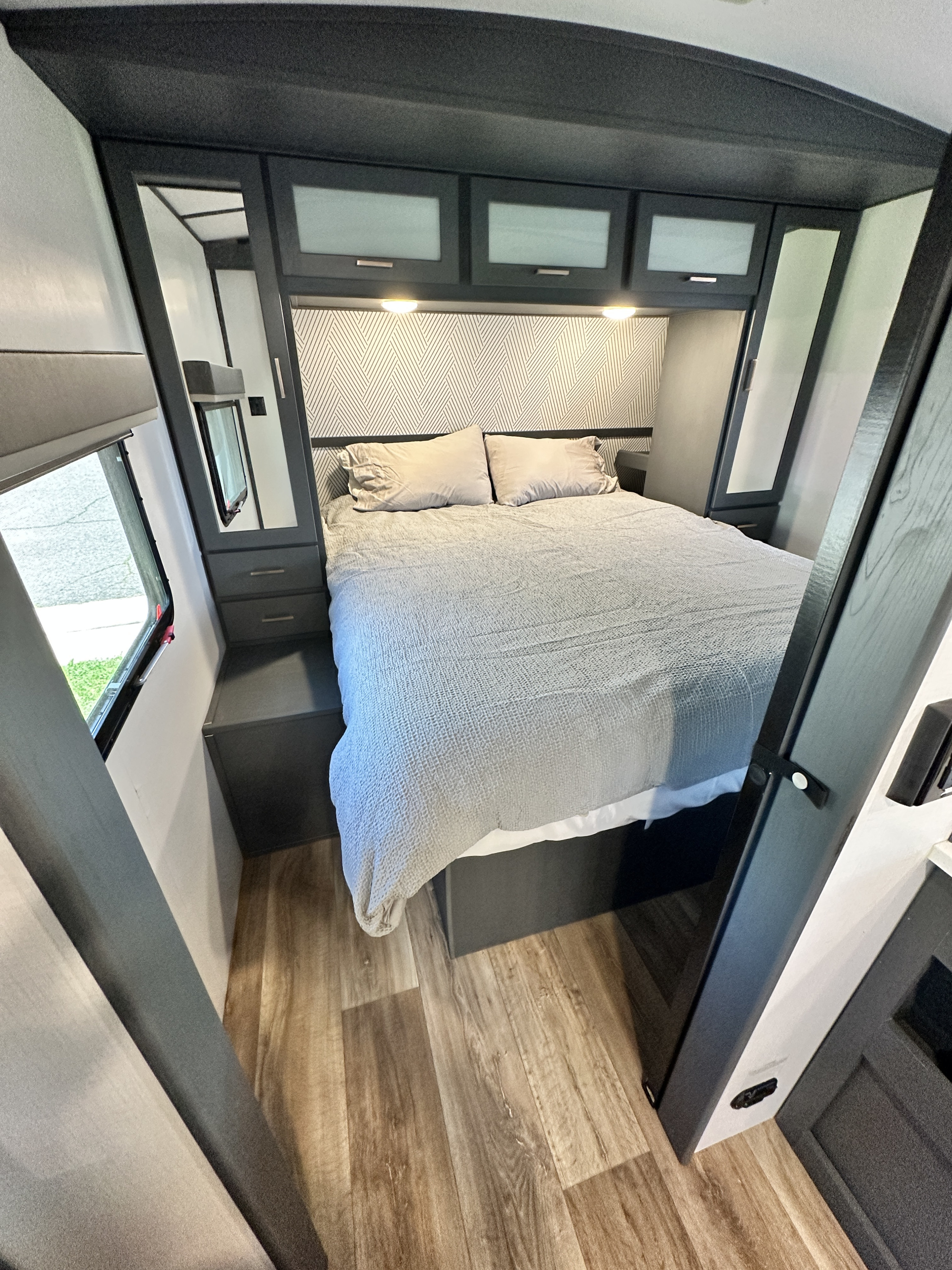 Cozy RV rental bedroom with a large bed, modern gray cabinets, patterned headboard, and wood-look flooring.. Keystone Premier 29BHPR 2022