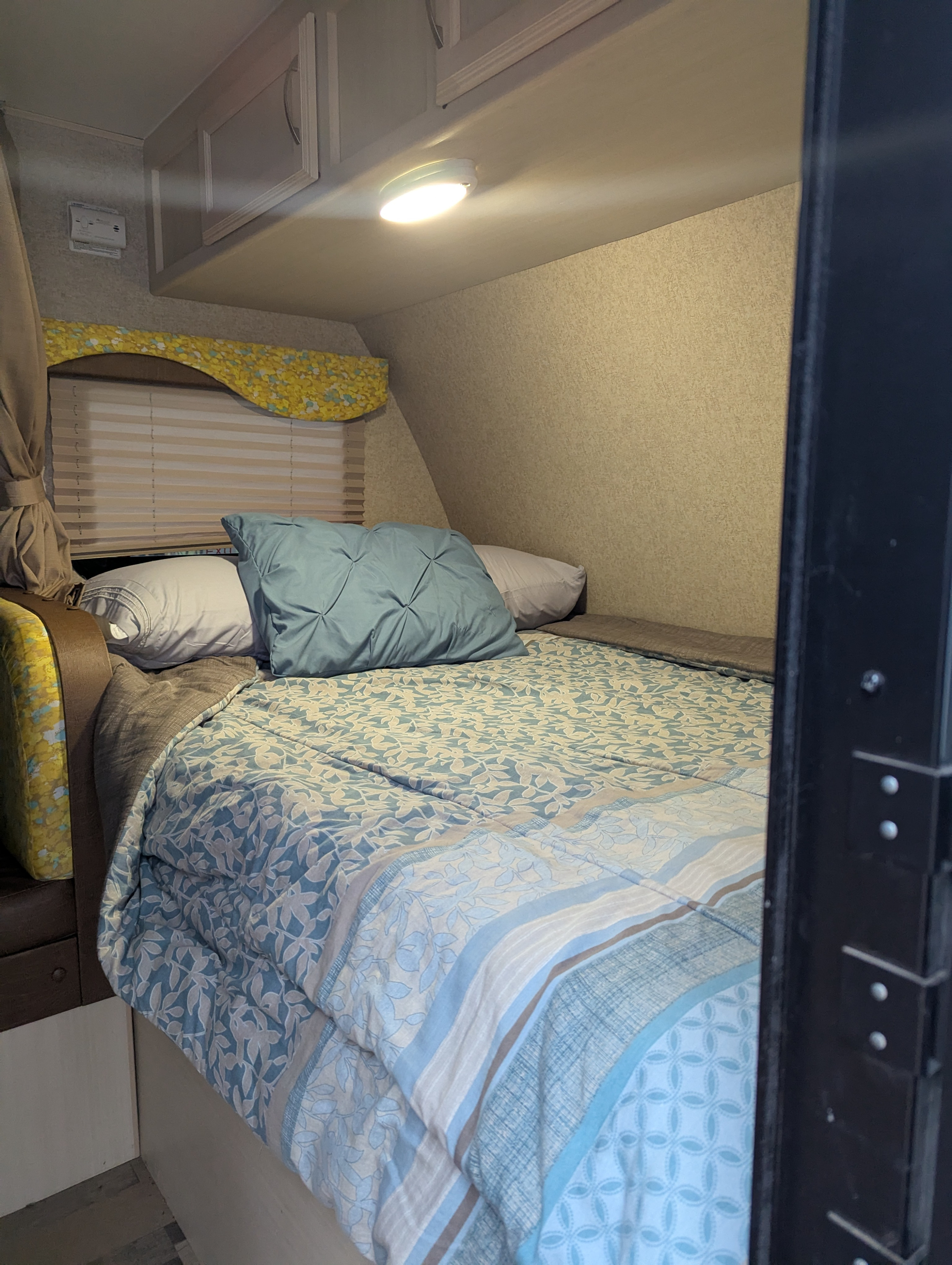 This RV rental features a cozy bedroom with blue patterned bedding, overhead cabinets, and a window with blinds.. Winnebago Minnie Winnie 2017