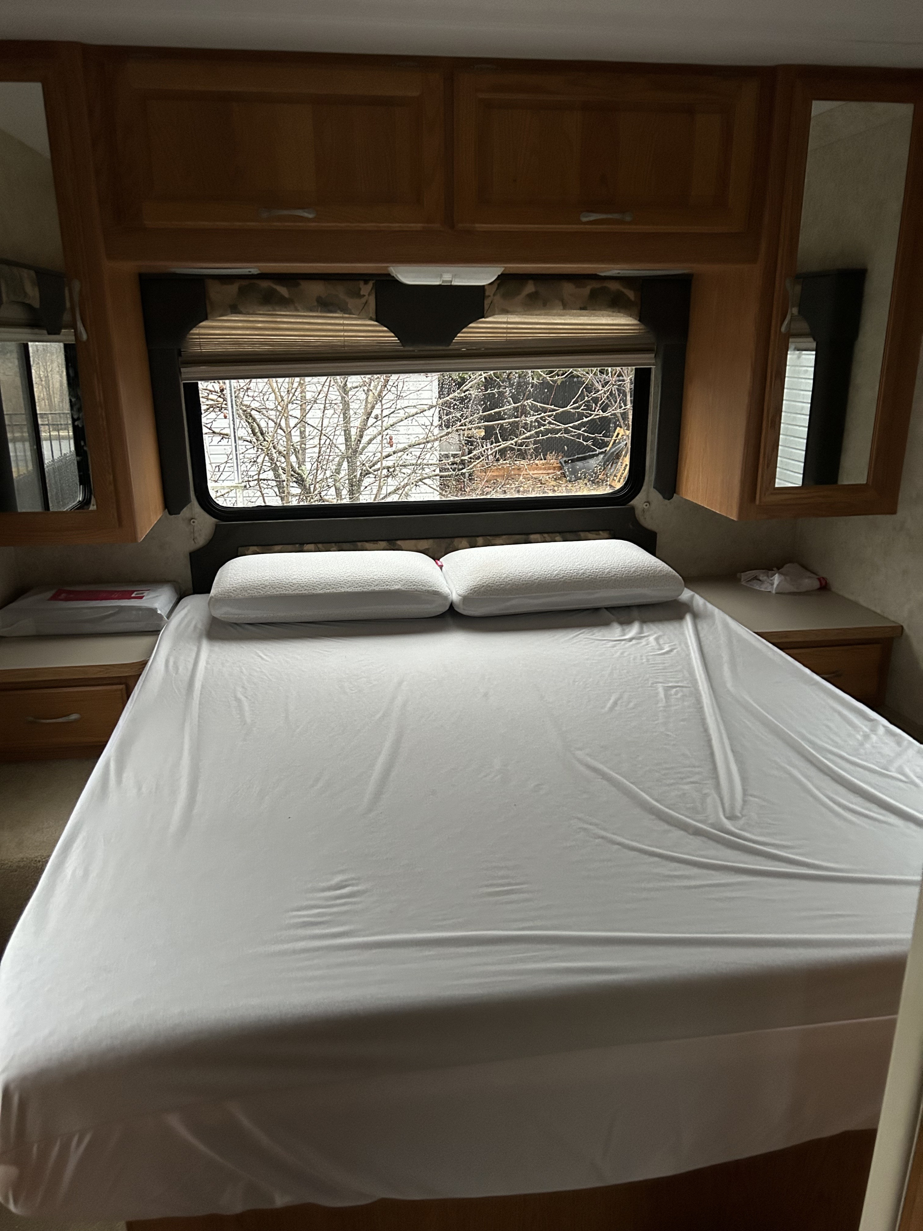 RV rental bedroom features a made bed with white sheets & pillows, wood cabinets, and a window overlooking bare trees.. Four Winds Hurricane 2006