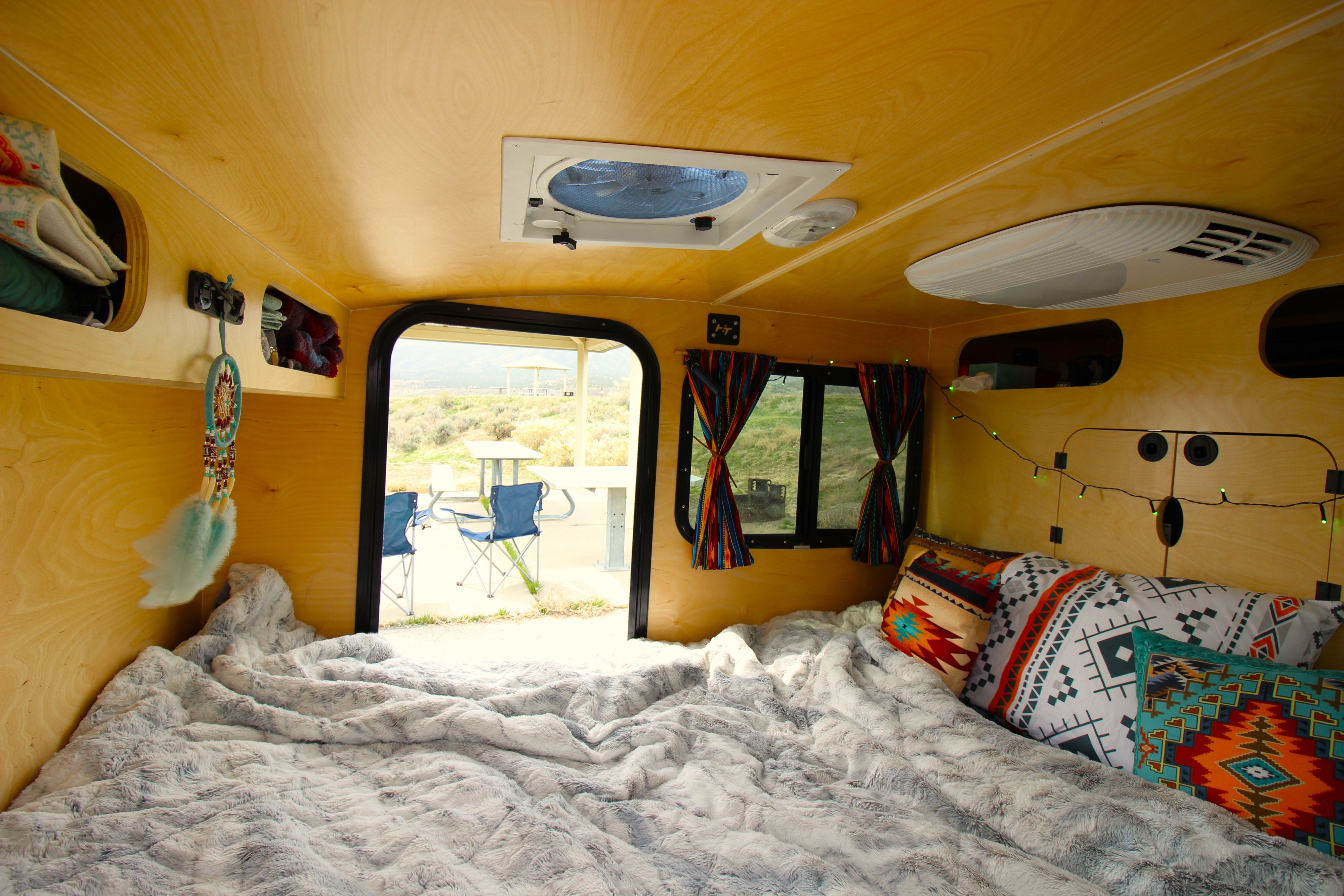 Cozy RV rental interior with a comfy bed, colorful pillows, and a scenic outdoor view. Perfect for camping.. Hiker Trailer 5x8 Mid-Range 2021