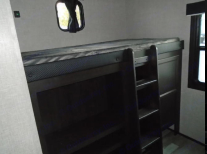 Compact RV rental sleeping area: a dark bunk bed with ladder, shelves below, and two windows, ideal for travel.. Jayco Jayflight 2023