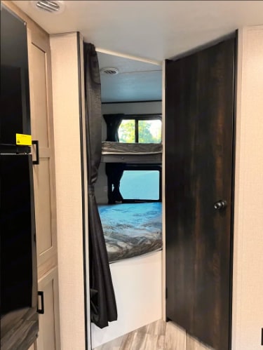 Inside an RV rental, a view into a bunk room with two beds, a window, and a privacy curtain. Ideal for families.. Starcraft Autumn Ridge 2024