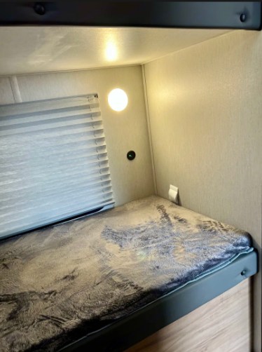 RV rental bunk bed: a cozy sleeping nook with window blinds, a wall light, and a patterned mattress for travel comfort.. Forest River cherokee Grey Wolf 2024