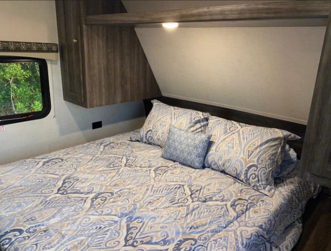 Comfortable RV rental bedroom featuring blue patterned bedding, overhead storage, and an exterior window view.. Starcraft Autumn Ridge 2020