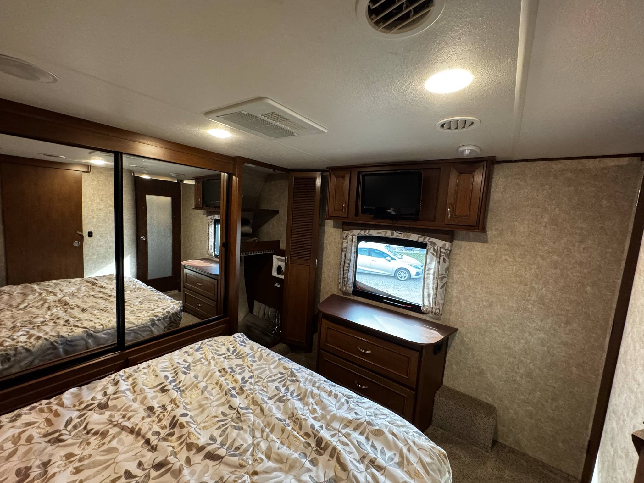 RV rental bedroom: Features a comfortable bed, mirrored closet, wall-mounted TV, and window.. Highland Ridge RV Mesa Ridge 2017