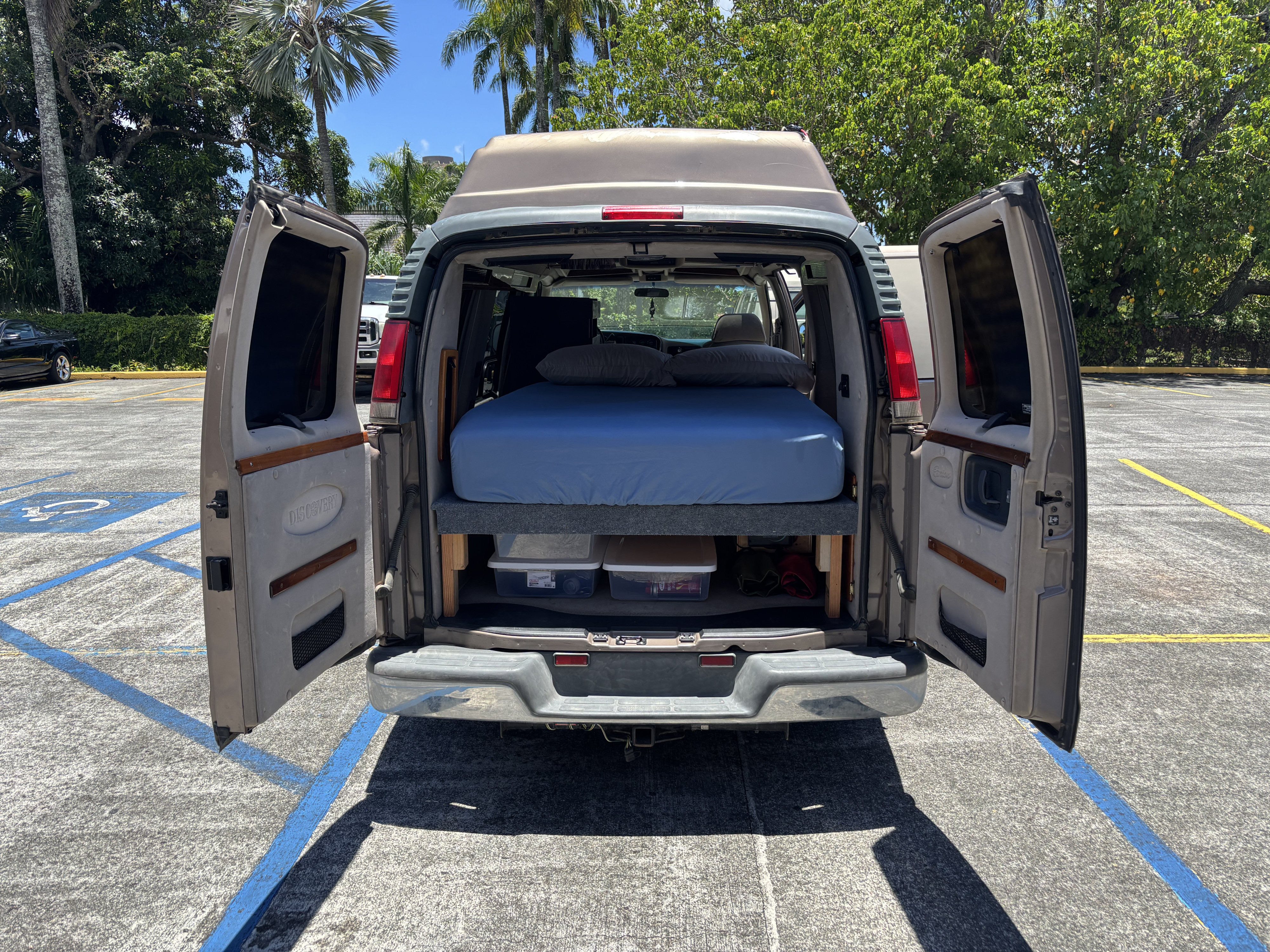 Rear view of an RV rental conversion van with open doors, showing a comfortable bed and storage inside. Ideal for travel.. Chevrolet Express G1500 1998