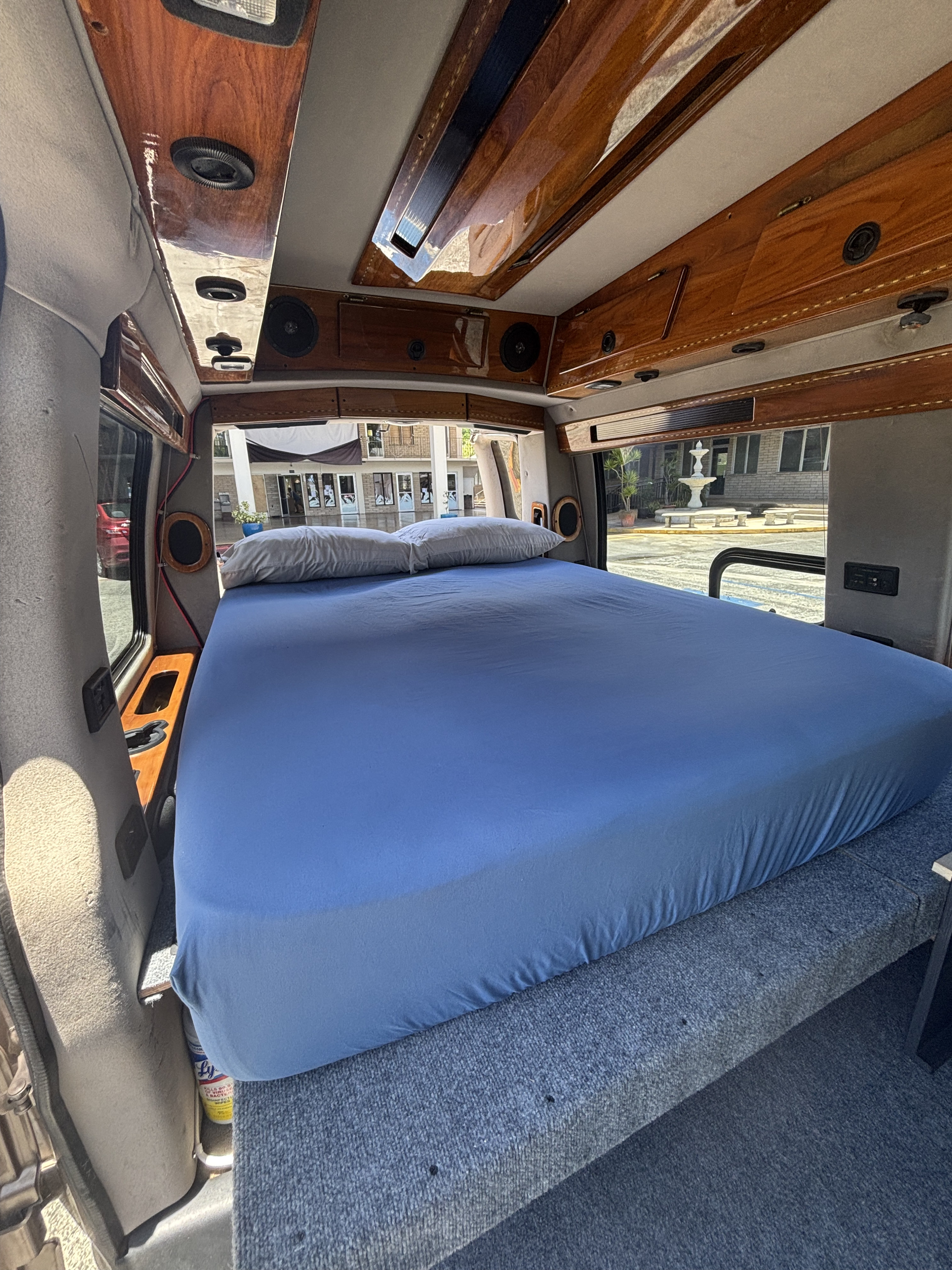 RV rental interior: A large bed with blue sheets, polished wood ceiling, and a fountain view outside.. Chevrolet Express G1500 1998