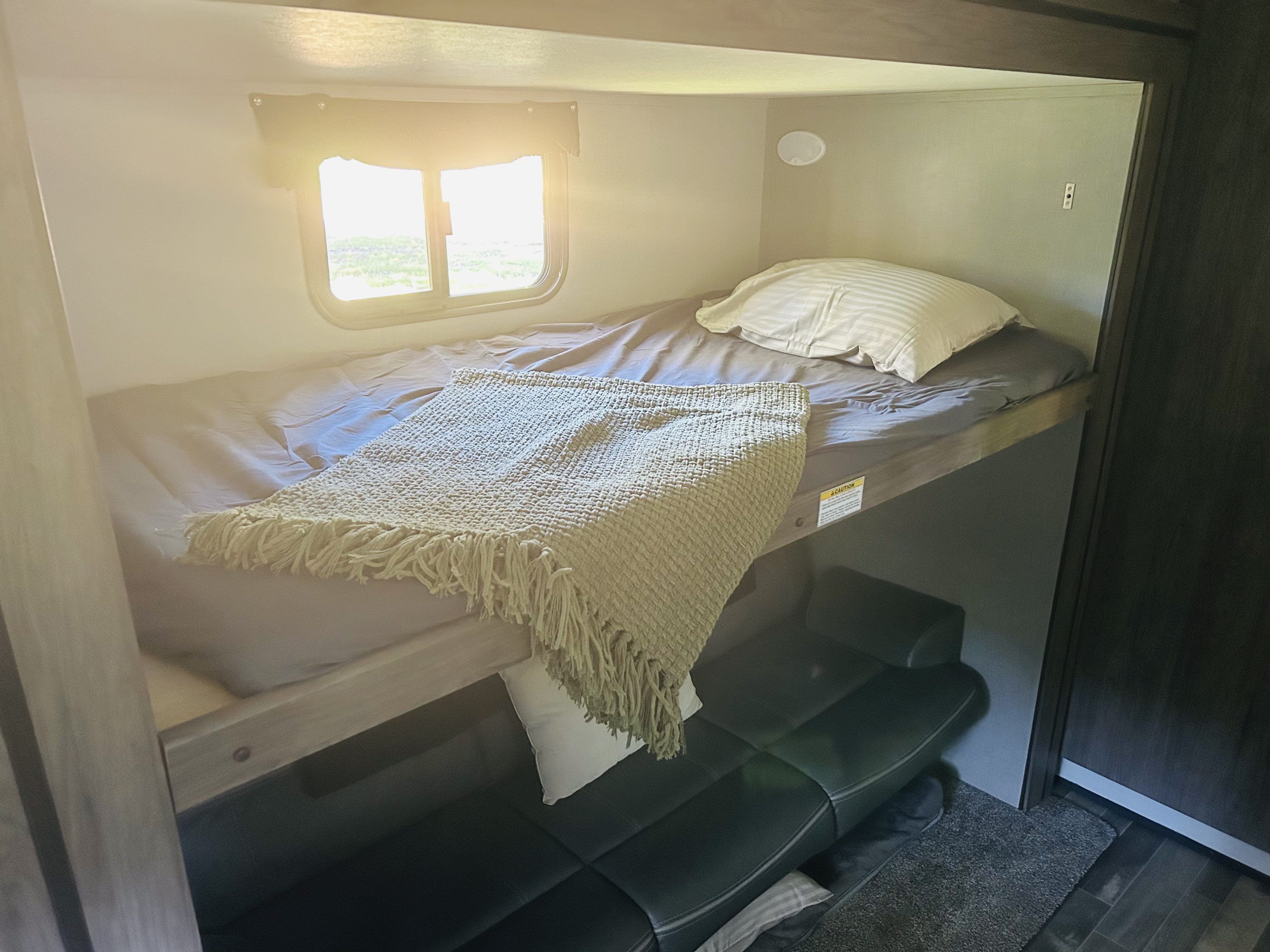 Cozy RV rental interior: a bunk bed with a window and a sofa bed below, illuminated by bright sunlight.. Crossroads RV Zinger 2020