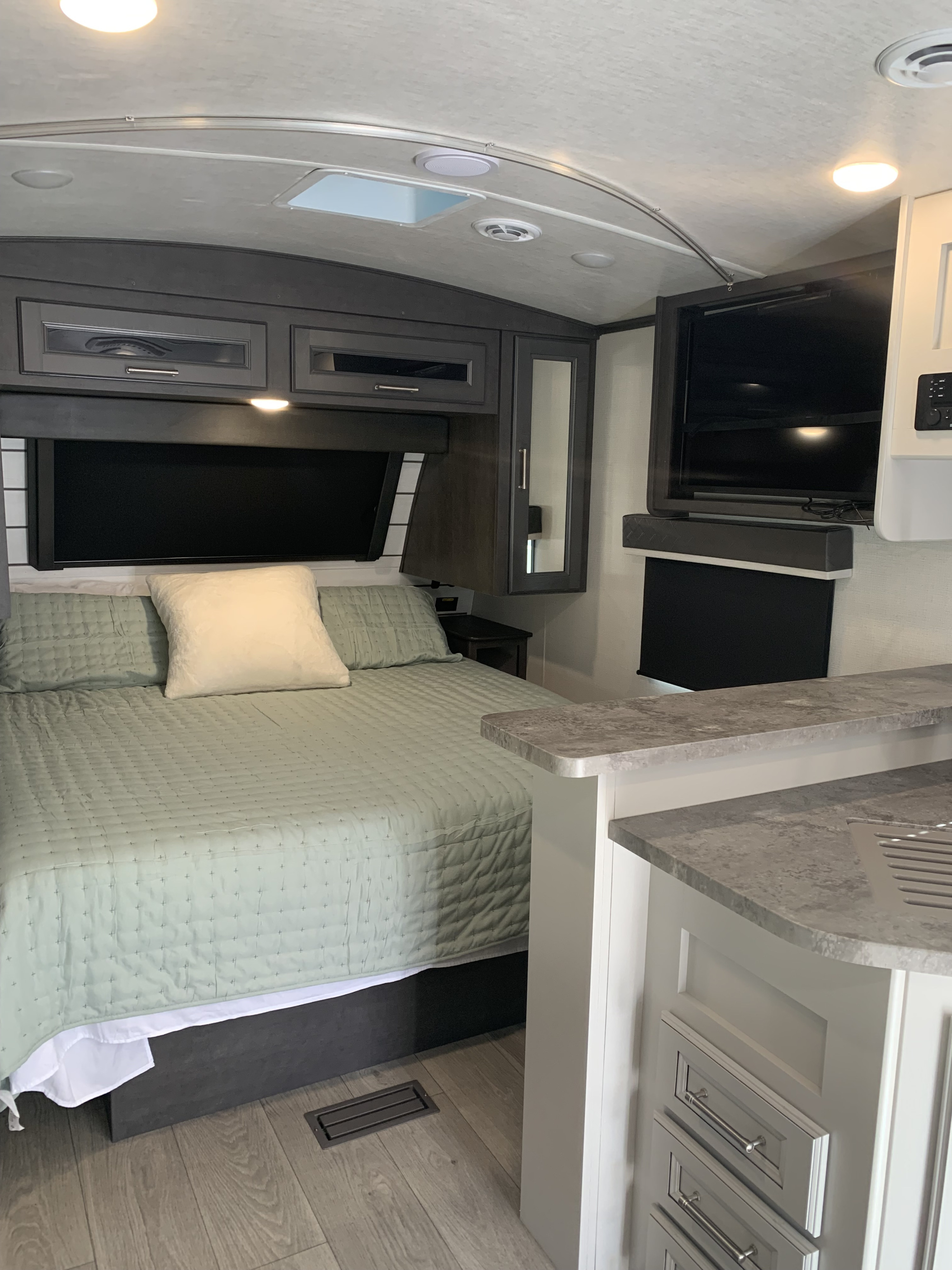 Experience comfort in this RV rental's inviting interior, showcasing a neatly made bed, entertainment setup, and stylish countertop.. Keystone RV Cougar 2024