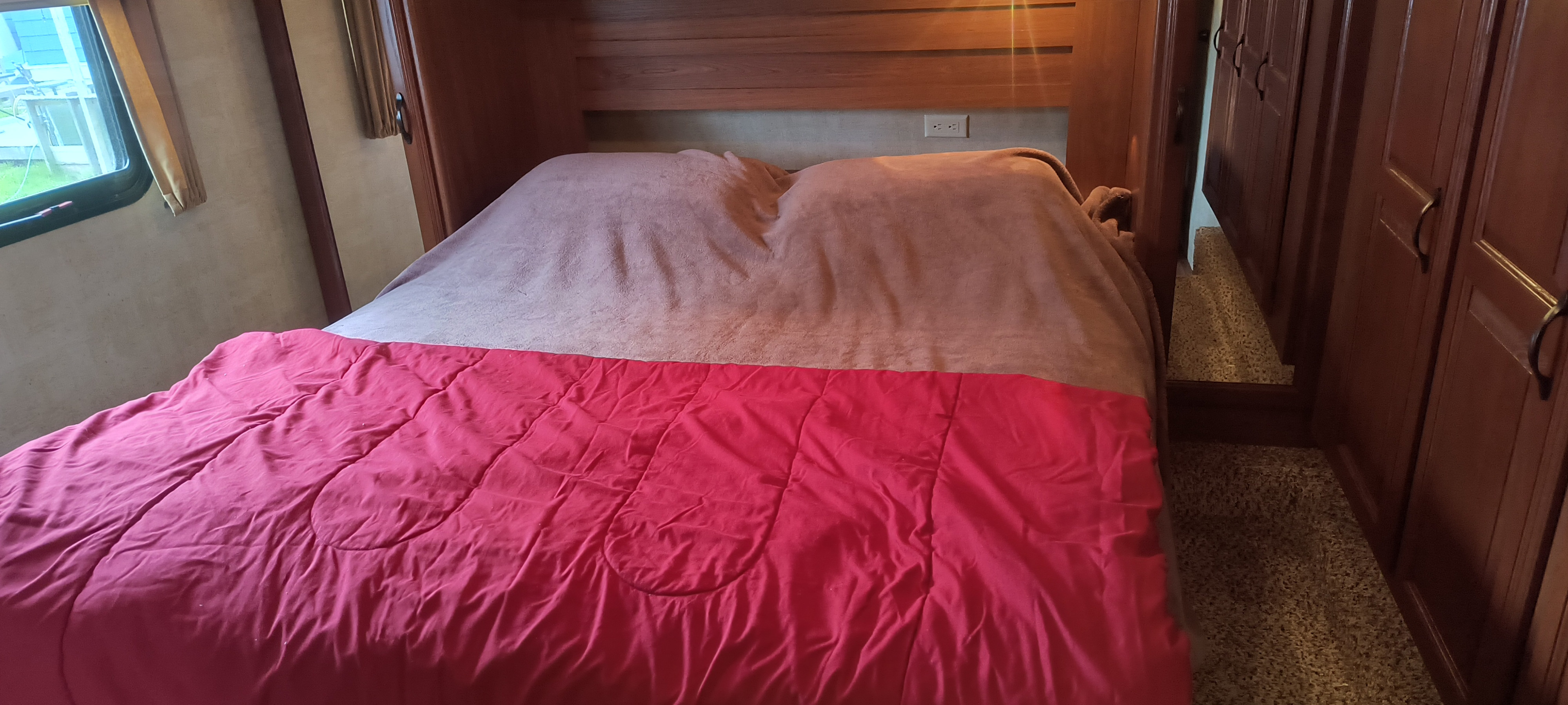 RV rental bedroom with a bed featuring a red comforter, light blanket, wood headboard, and window.. Keystone RV Sydney 10th Anniversary 2012