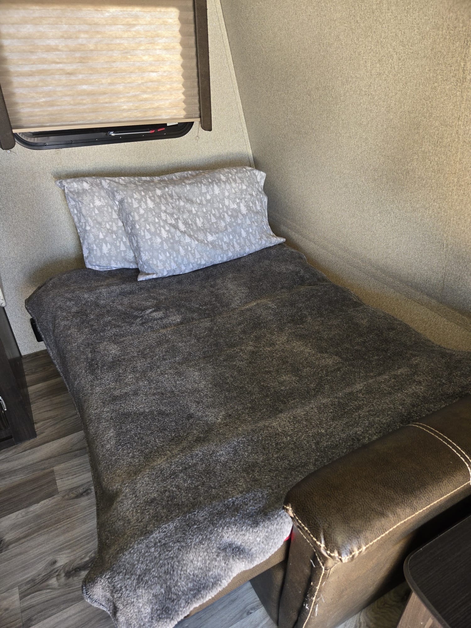 Compact RV rental sleeping area: bed with gray blanket & tree pillows, window, textured walls, wood floor.. Keystone RV Springdale 2018