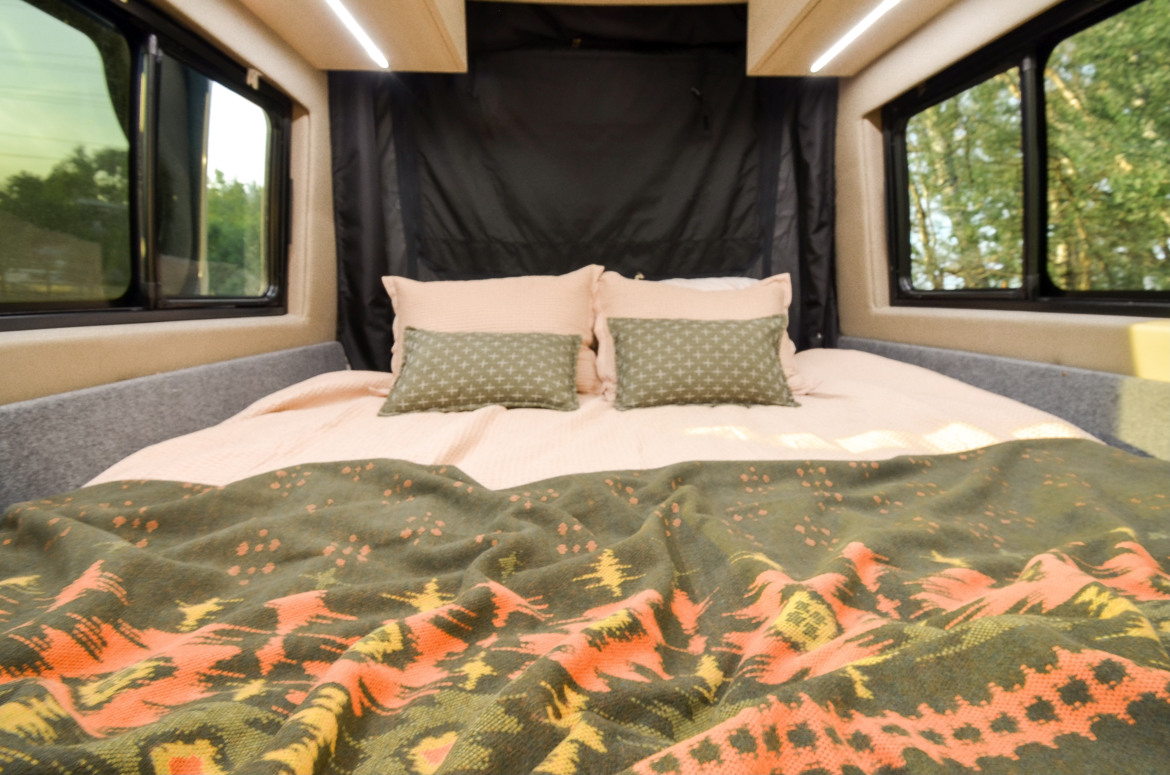Comfortable RV rental bedroom featuring a full bed with cozy pink sheets, patterned pillows, and scenic window views.. Cahaba Cahaba Class B 2021