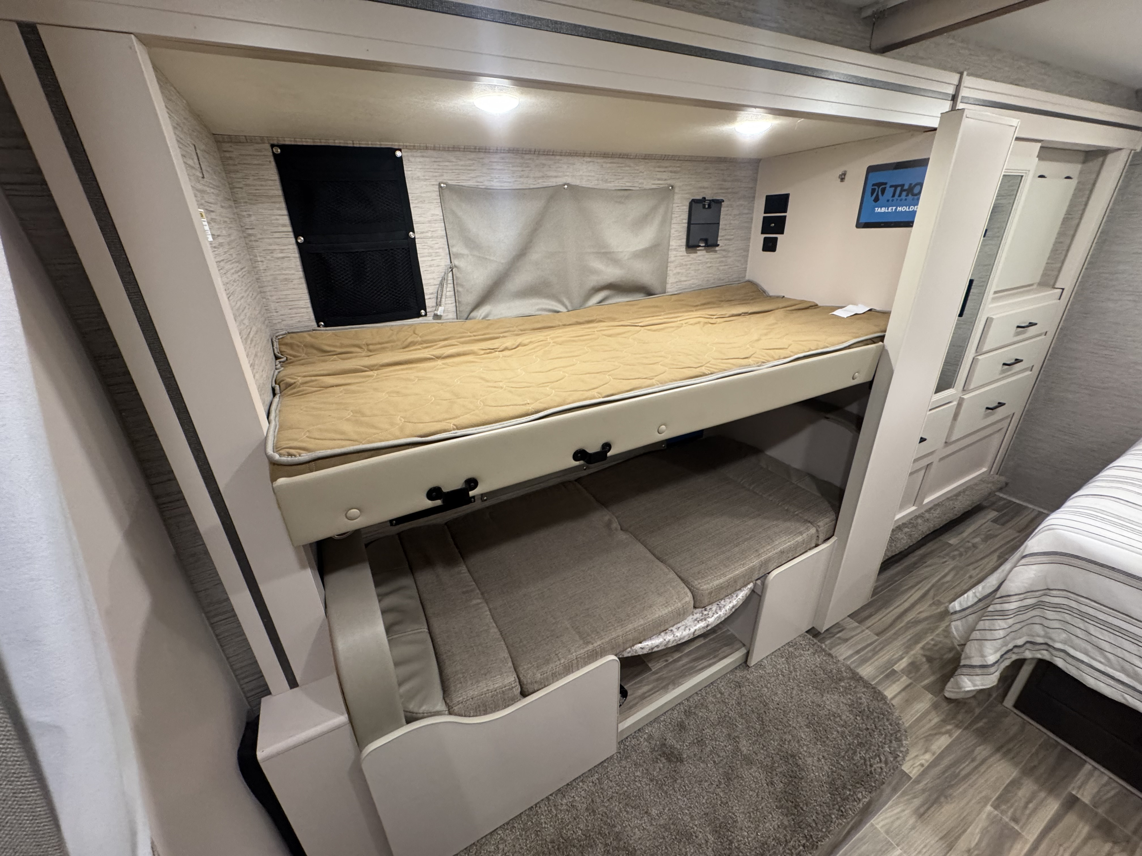 Inside an RV rental: a modern bunk bed setup with a top bunk, convertible lower seating/bed, and cabinet storage.. Thor Freedom Elite 2022