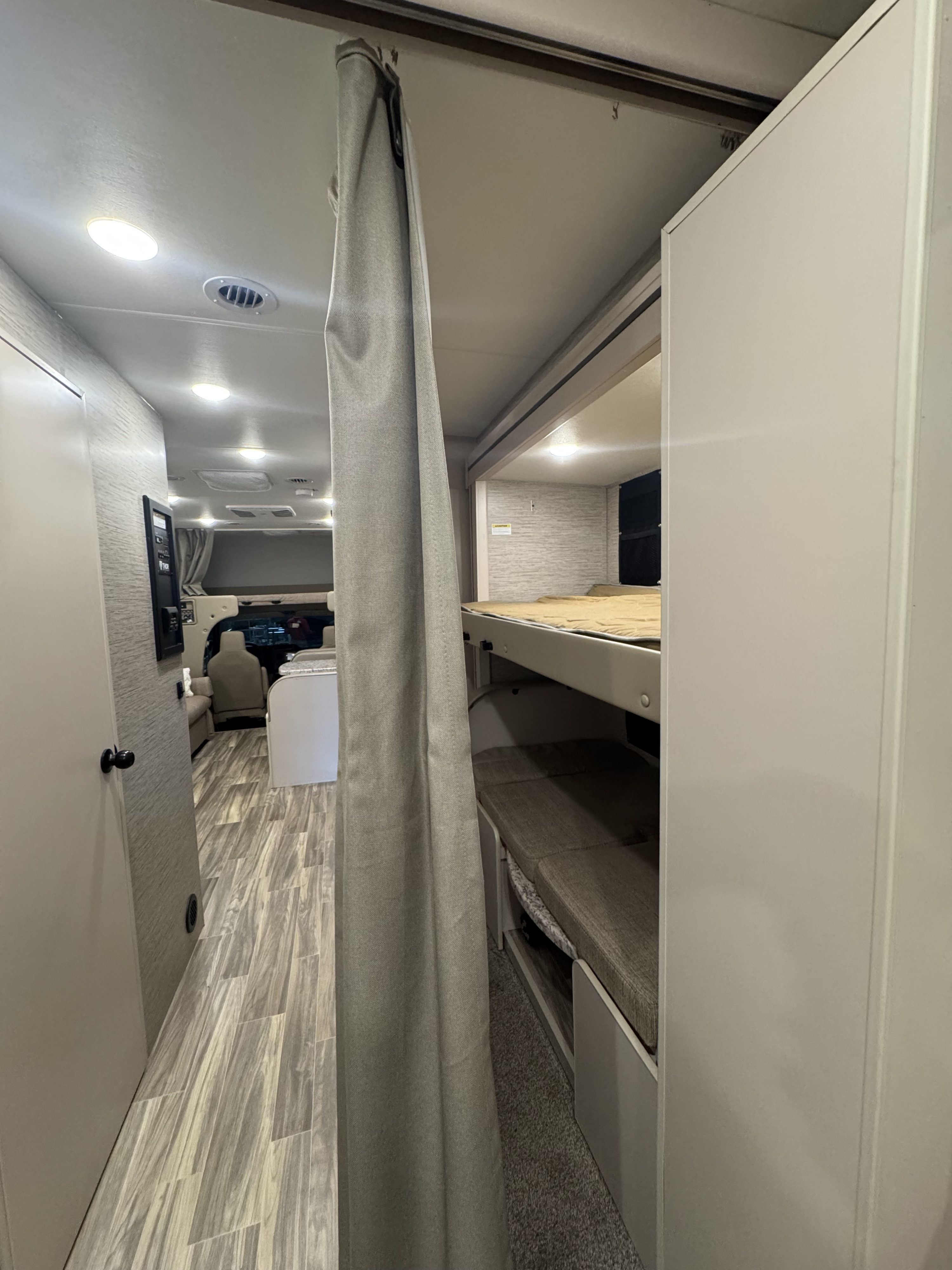 RV rental interior with bright lights, wood-look floor, and a bunk bed area separated by a gray curtain for family travel.. Thor Freedom Elite 2022
