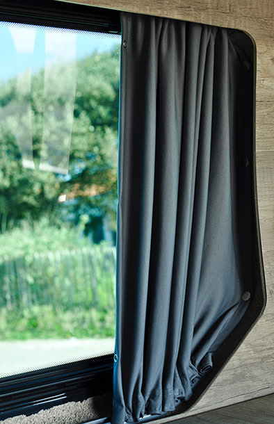 RV rental window with a dark gray privacy curtain, partially open to show green trees outside.. Renault TRAFIC 2024