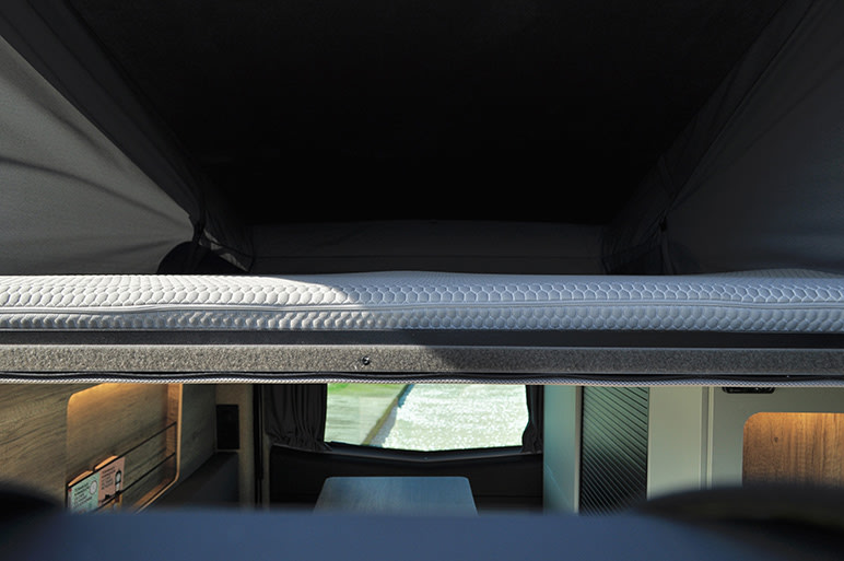 Inside an RV rental: a comfortable pop-top bed overlooks the main cabin and a window view of water. Perfect for travel.. Renault TRAFIC 2024