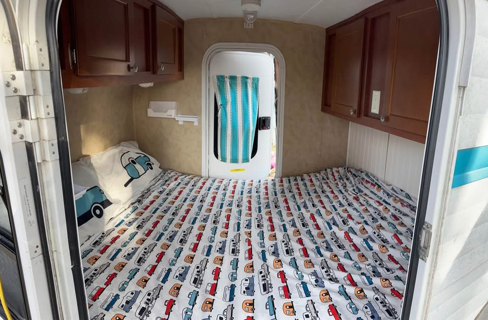 RV rental bedroom view: A cozy camper interior with a full bed, fun patterned sheets, and overhead storage.. Riverside RV White Water 2014