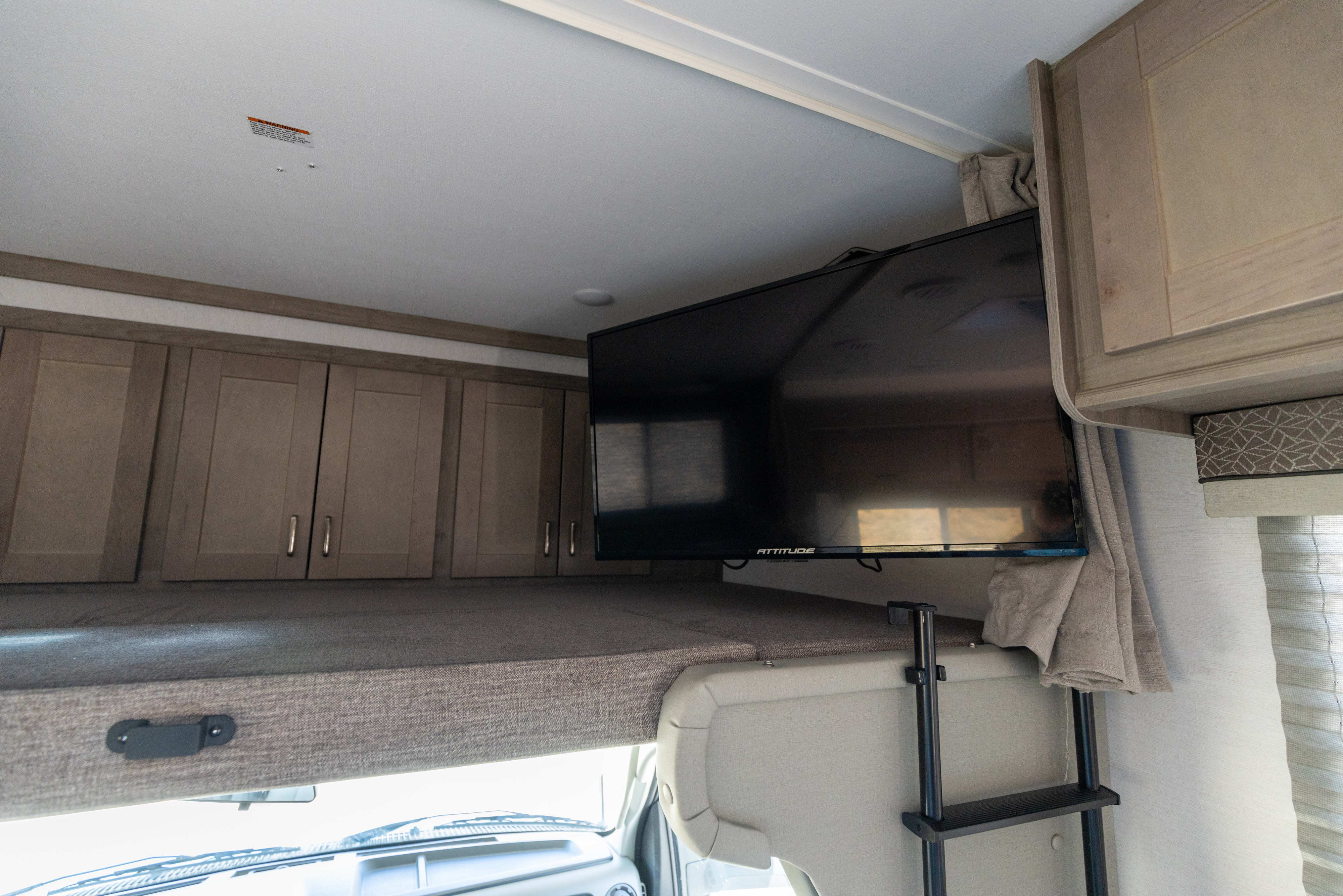 Inside an RV rental: a comfortable cab-over bunk area with a mounted TV, storage cabinets, and a ladder.. Gulf Stream Conquest 2024