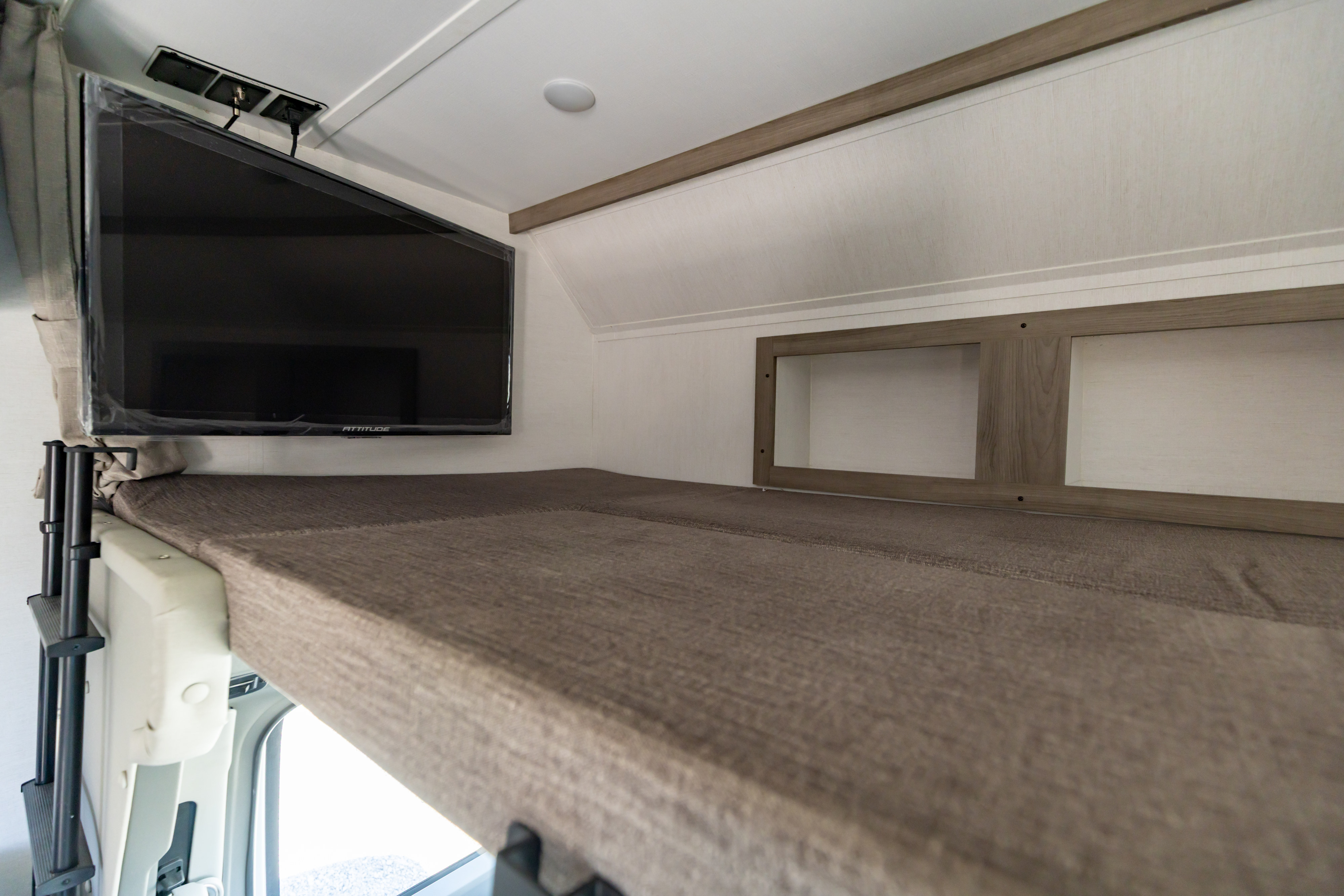 Inside an RV rental: a comfortable bunk bed with a wall-mounted TV & storage cubbies.. Gulf Stream Conquest 2024