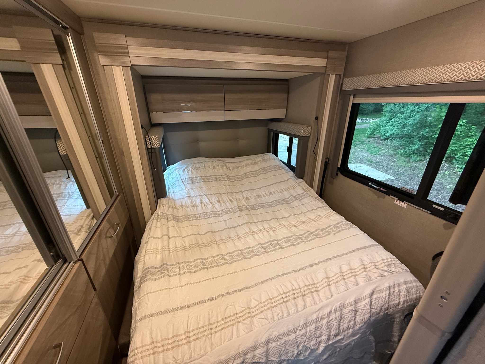 A cozy RV rental bedroom featuring a comfortable bed, overhead storage, and a refreshing window view.. Thor Tiburon 2021
