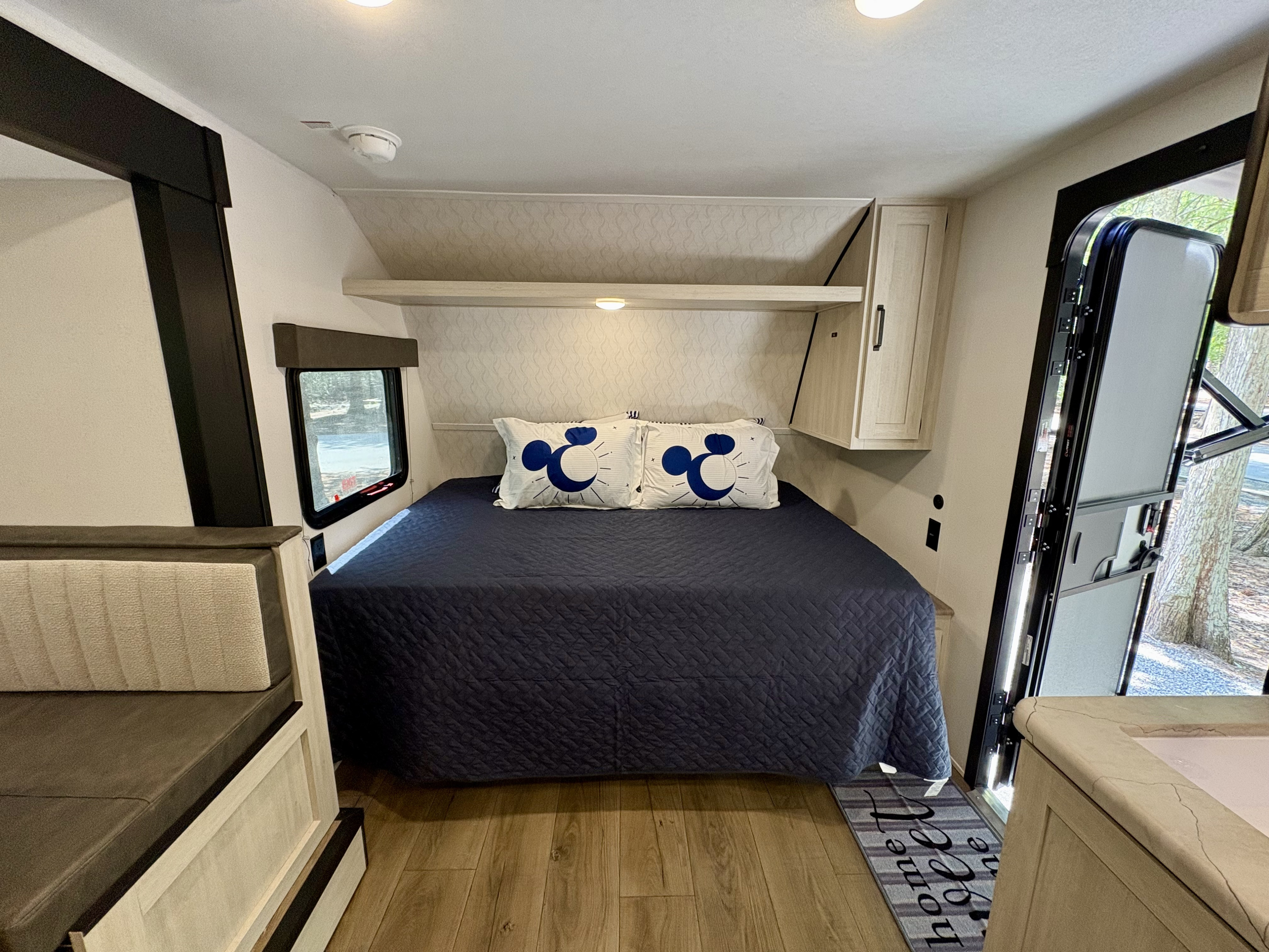 Inside a modern rv rental: a cozy bedroom area with a bed, Mickey pillows, and dinette. Features wood flooring & light decor.. Forest River Puma 2025