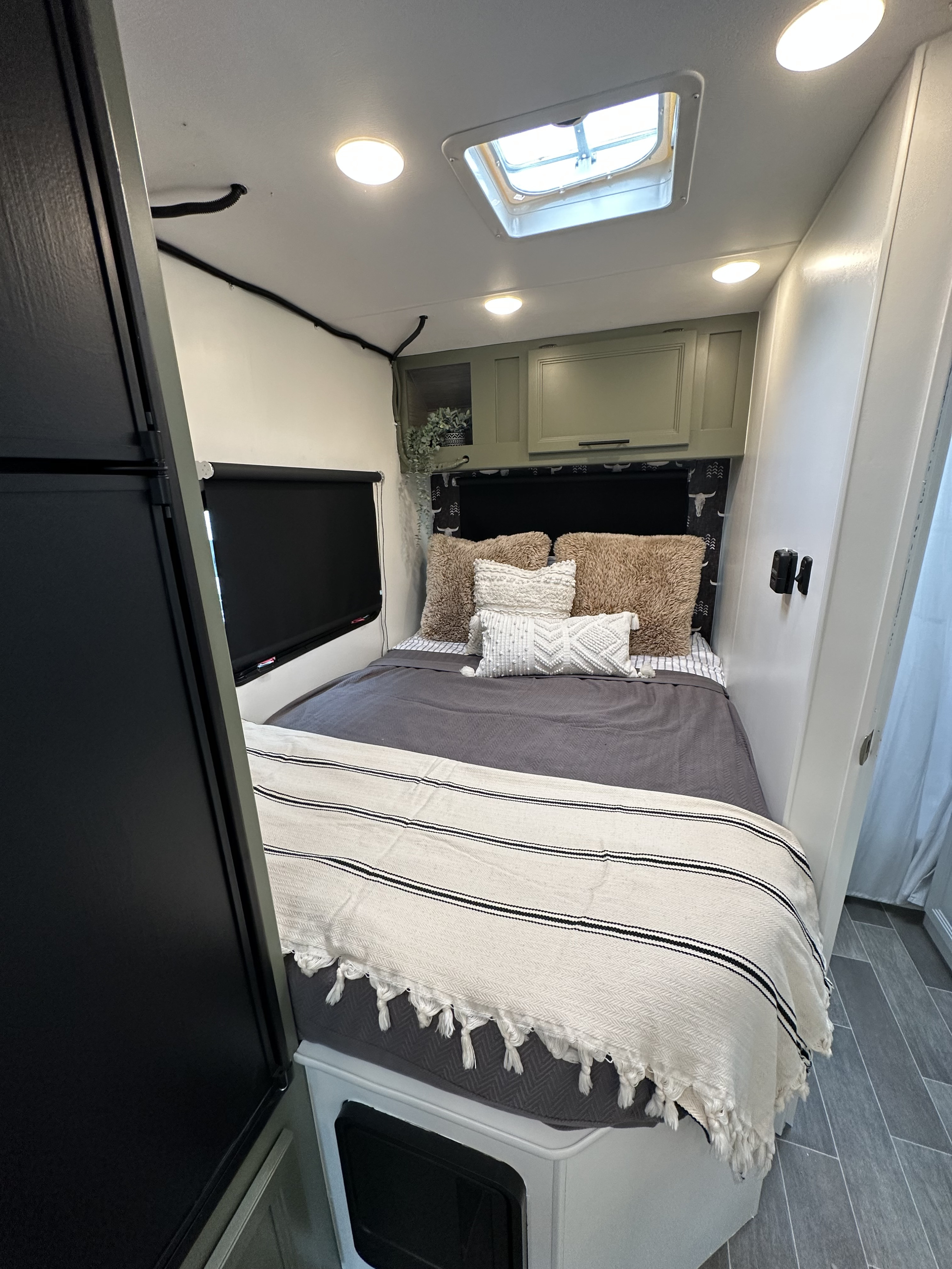 Modern RV rental bedroom boasts a cozy bed, sage overhead cabinets, ceiling lights, and a skylight for natural light.. Thor Chateau 2022