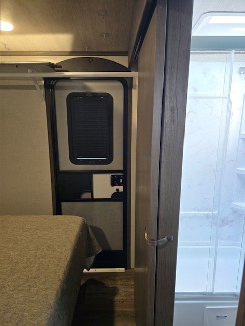 An RV rental interior reveals a bed on the left, main entry door in the center, and a compact shower stall on the right.. Keystone RV Cougar 2021